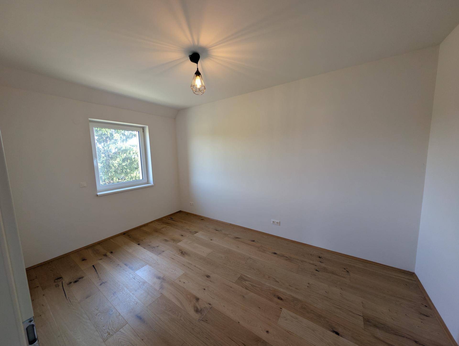 Helles Schlafzimmer mit Eichenparkett und Fenster, das einen Blick ins Grüne bietet.