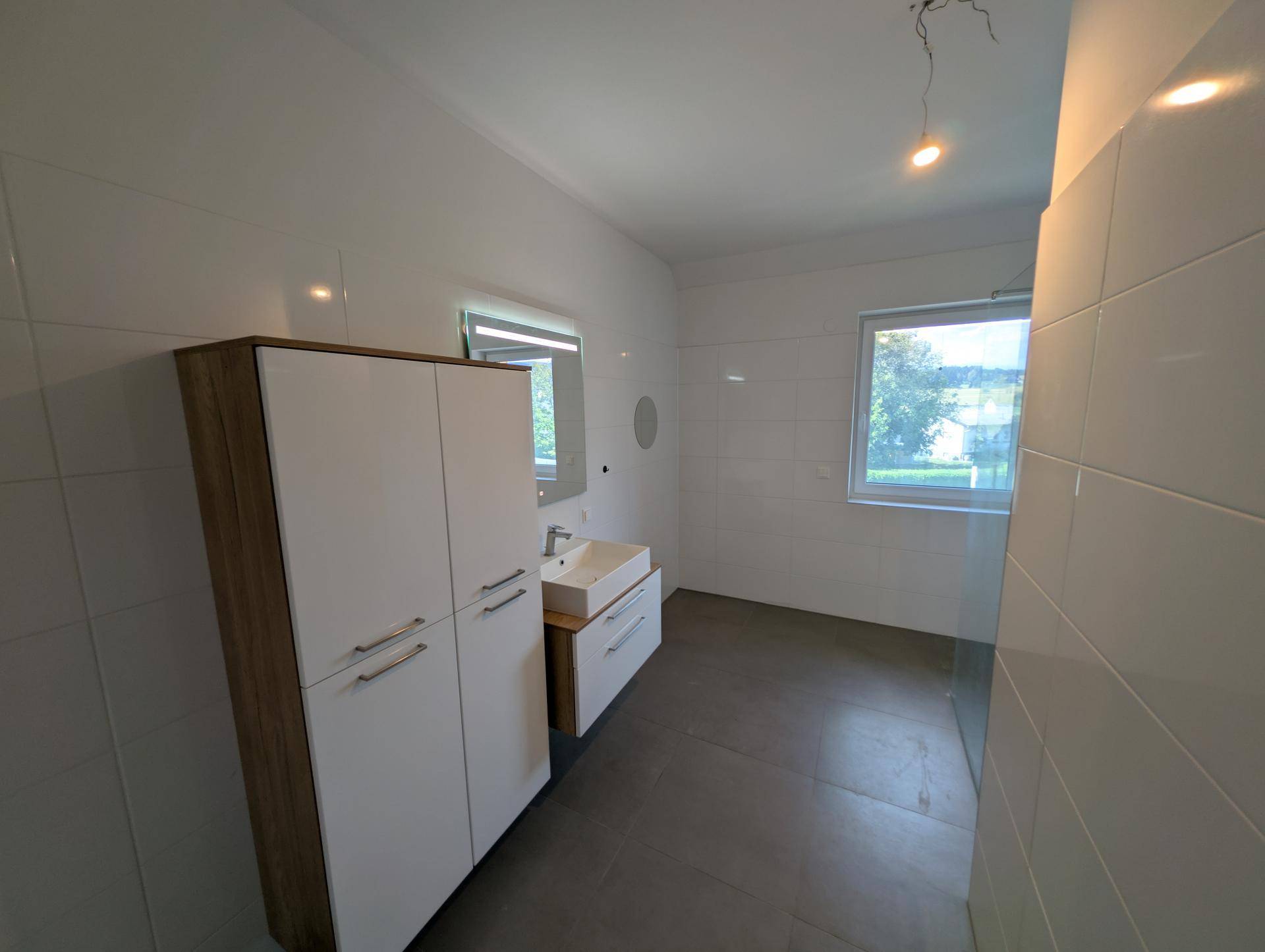 Modernes Badezimmer mit Einzelwaschbecken, großem Schrank und Fenster für Tageslicht.