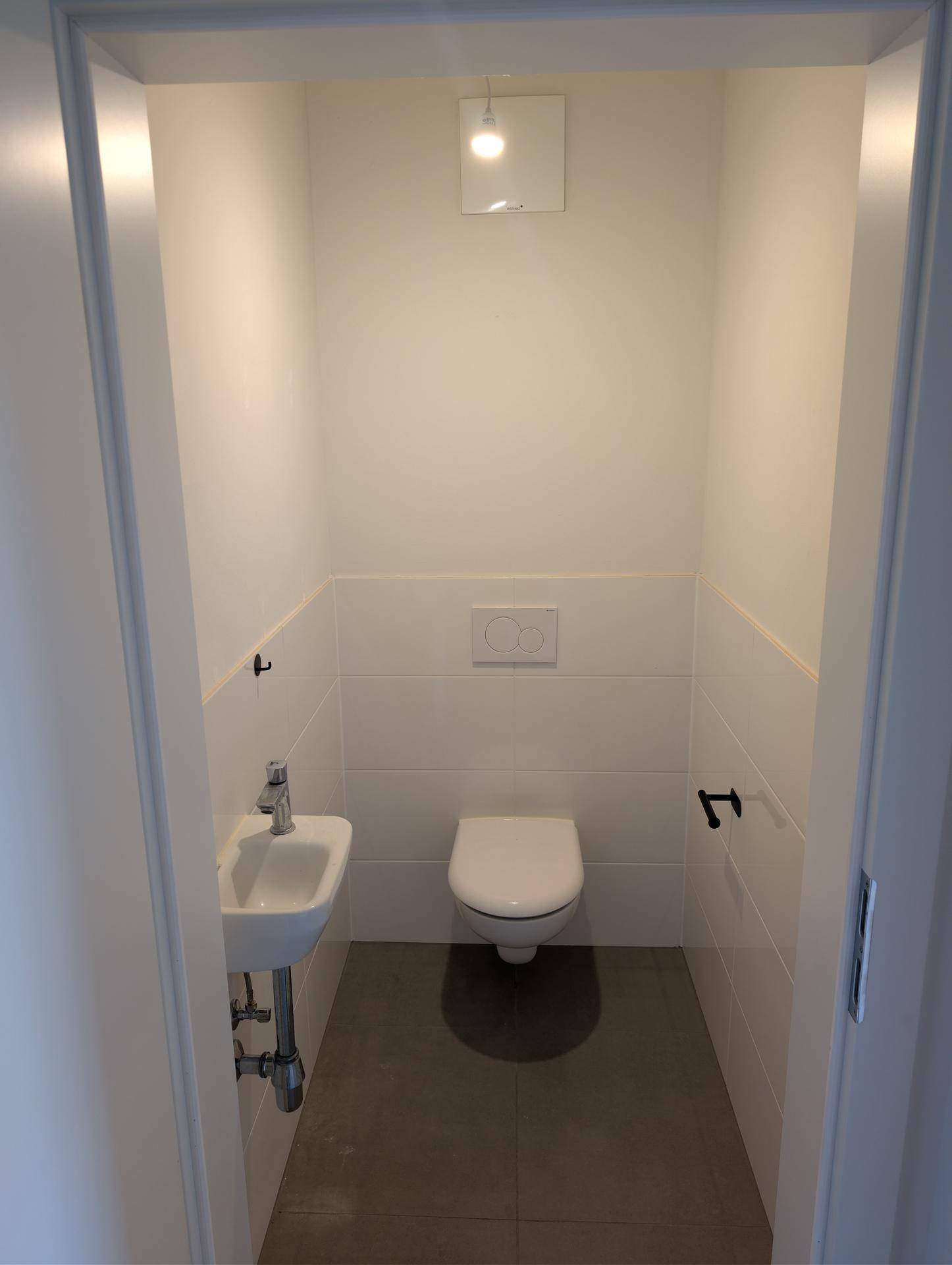 Kleines Gäste-WC mit wandhängendem WC, kleinem Waschbecken und modernen Fliesen.