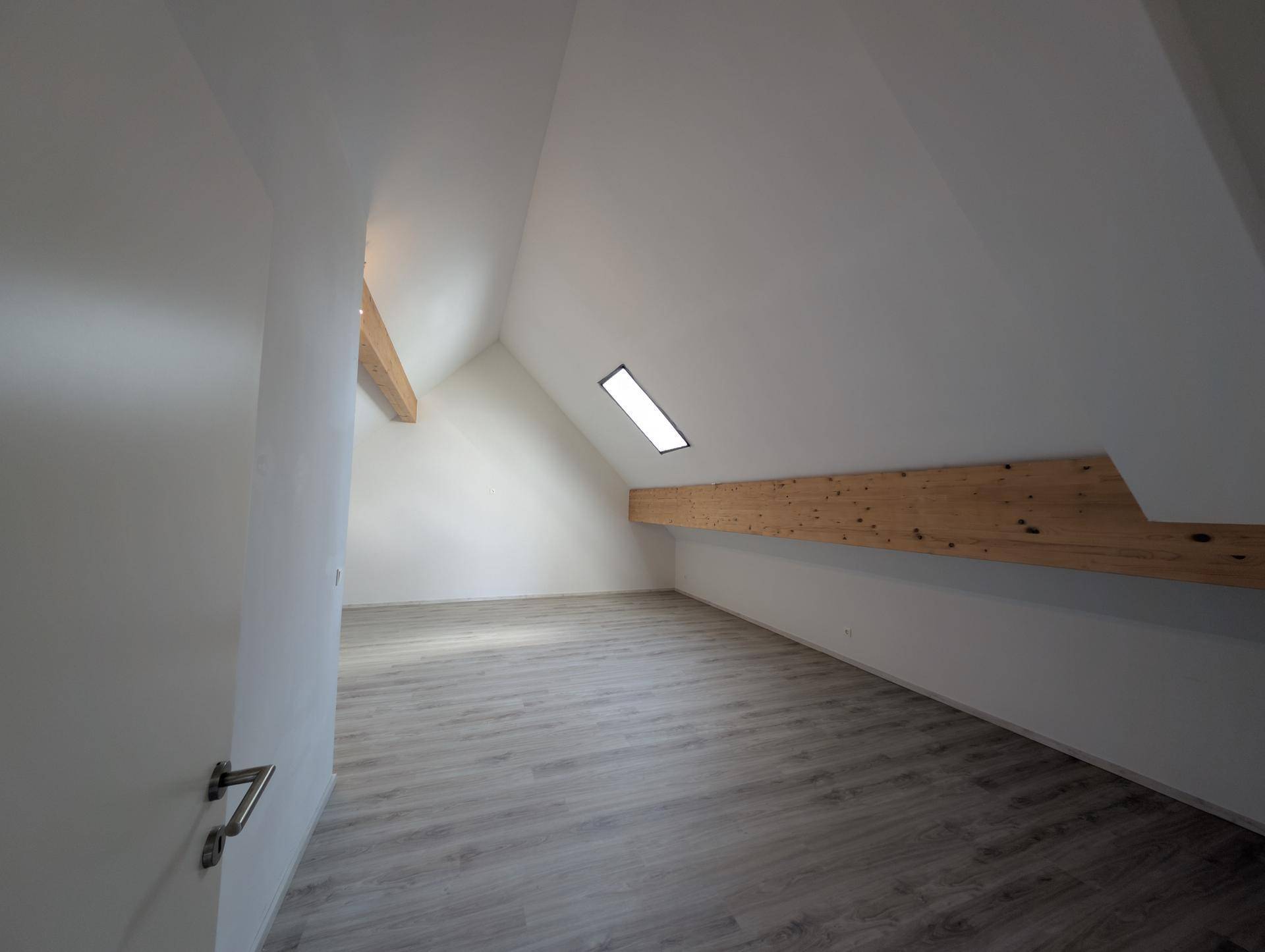 Geräumiger Dachbodenraum mit schrägen Decken, Dachfenster und sichtbaren Holzbalken.