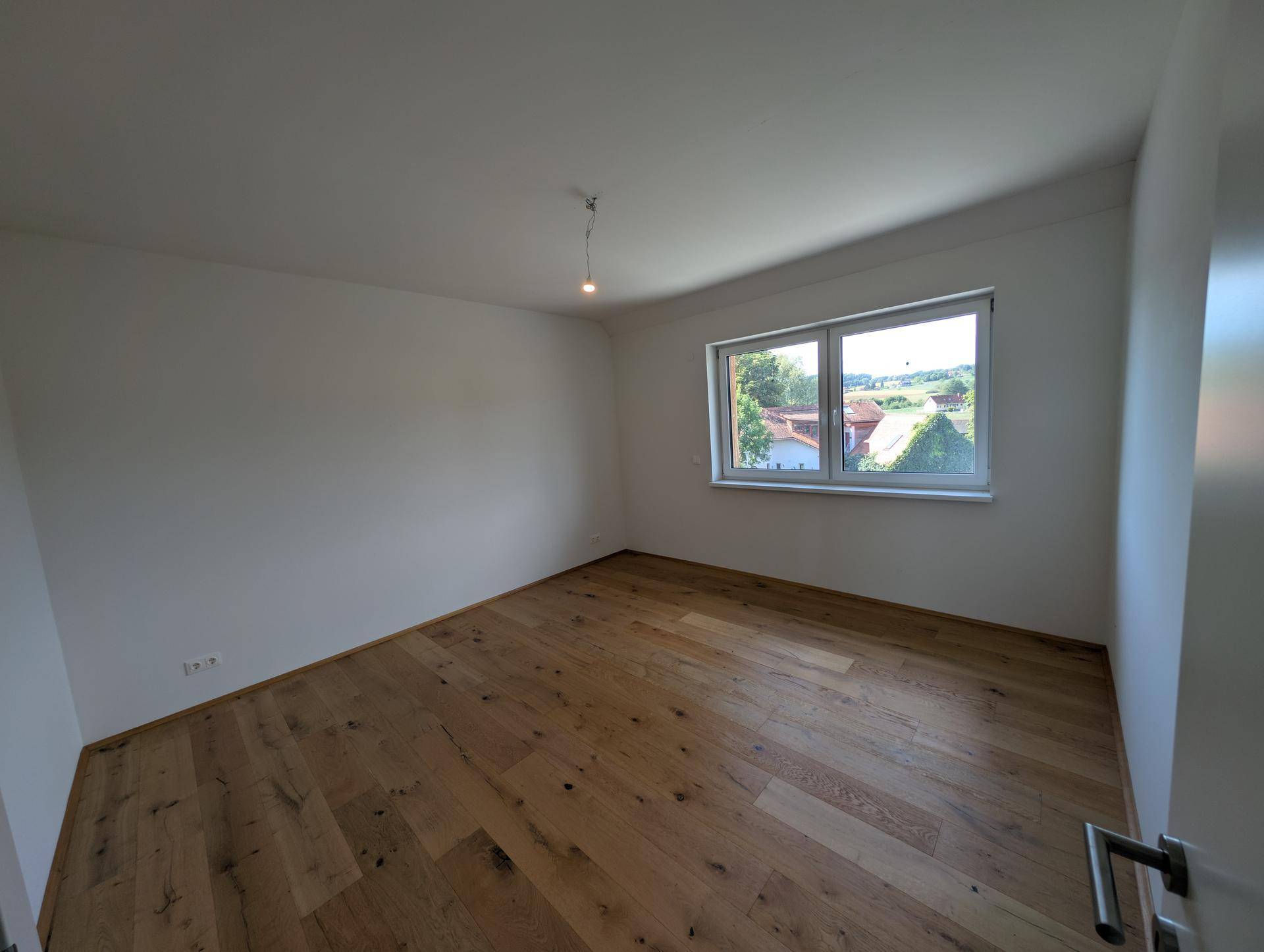 Geräumiges Schlafzimmer mit Holzboden und Fenster mit weitem Blick über die Landschaft.