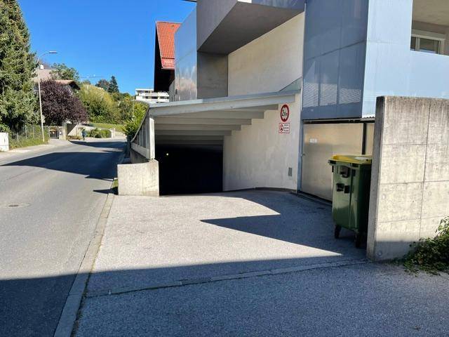 Einfahrt zu einer Tiefgarage unter einem modernen Gebäude mit klaren Linien und einem Mülltonnenbereich.