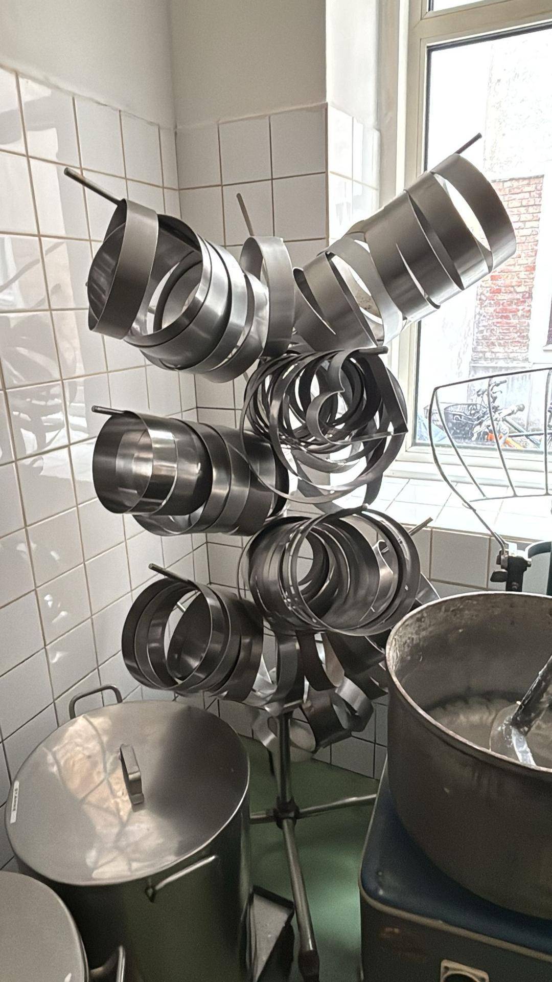 Metallbackformen hängen an einem Gestell neben einem Fenster in einer professionellen Küche mit weißen Fliesenwänden.