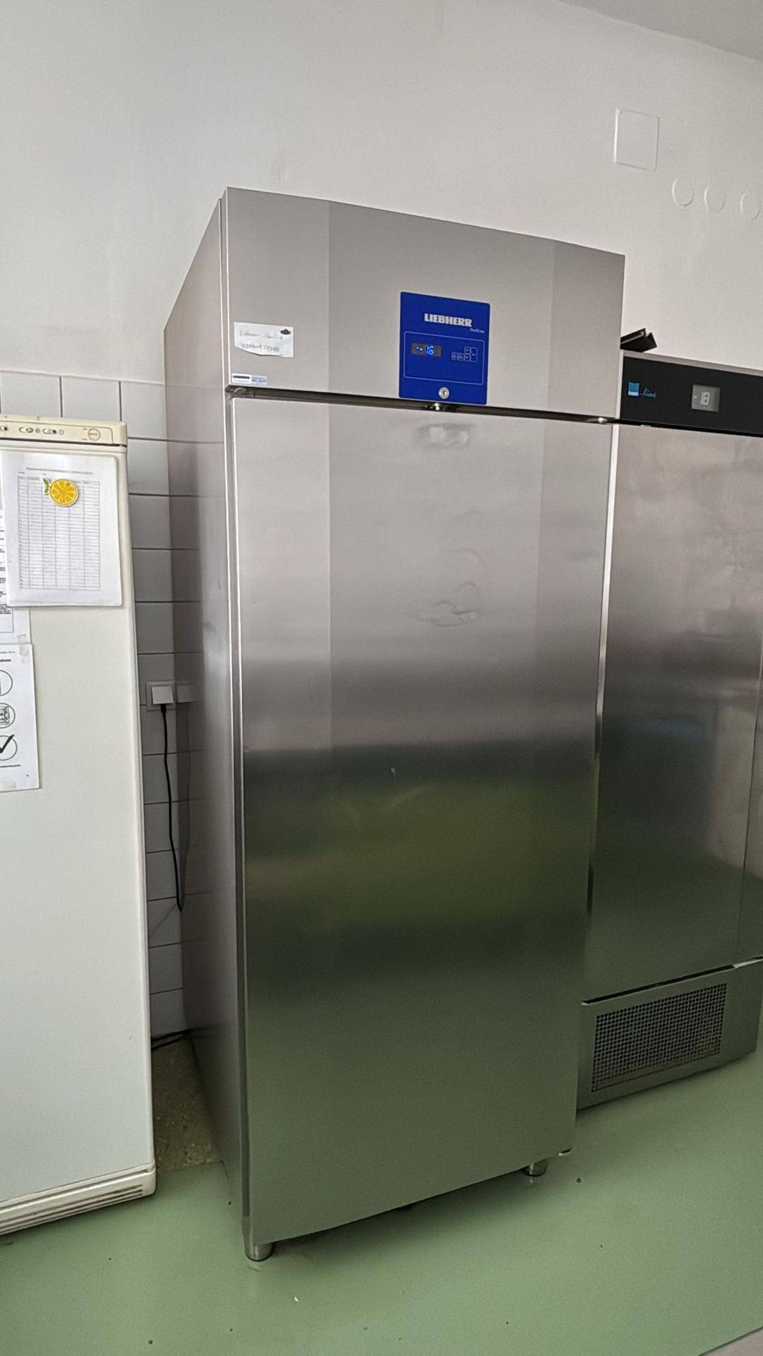 Großer Kühlschrank aus Edelstahl der Marke Liebherr in einer gewerblichen Küche mit gefliesten Wänden und grünem Boden.