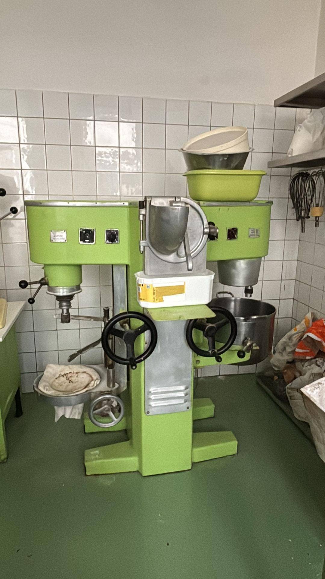 Große grüne Industriemaschine in einer professionellen Küche mit weißen Fliesenwänden und grünem Boden.