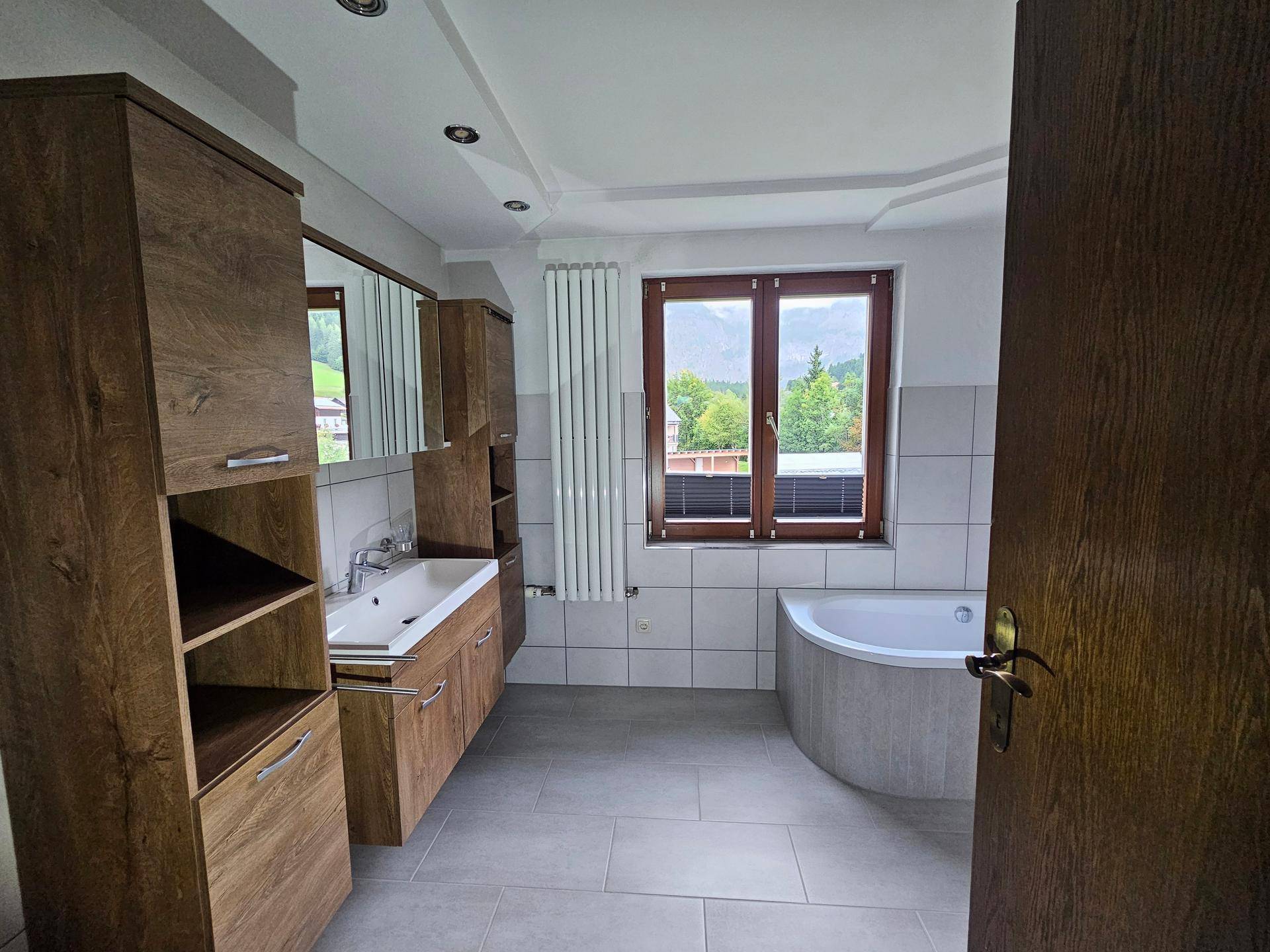 Modernes Badezimmer mit Holzwaschtisch, Eckbadewanne und Fenster mit Bergblick.