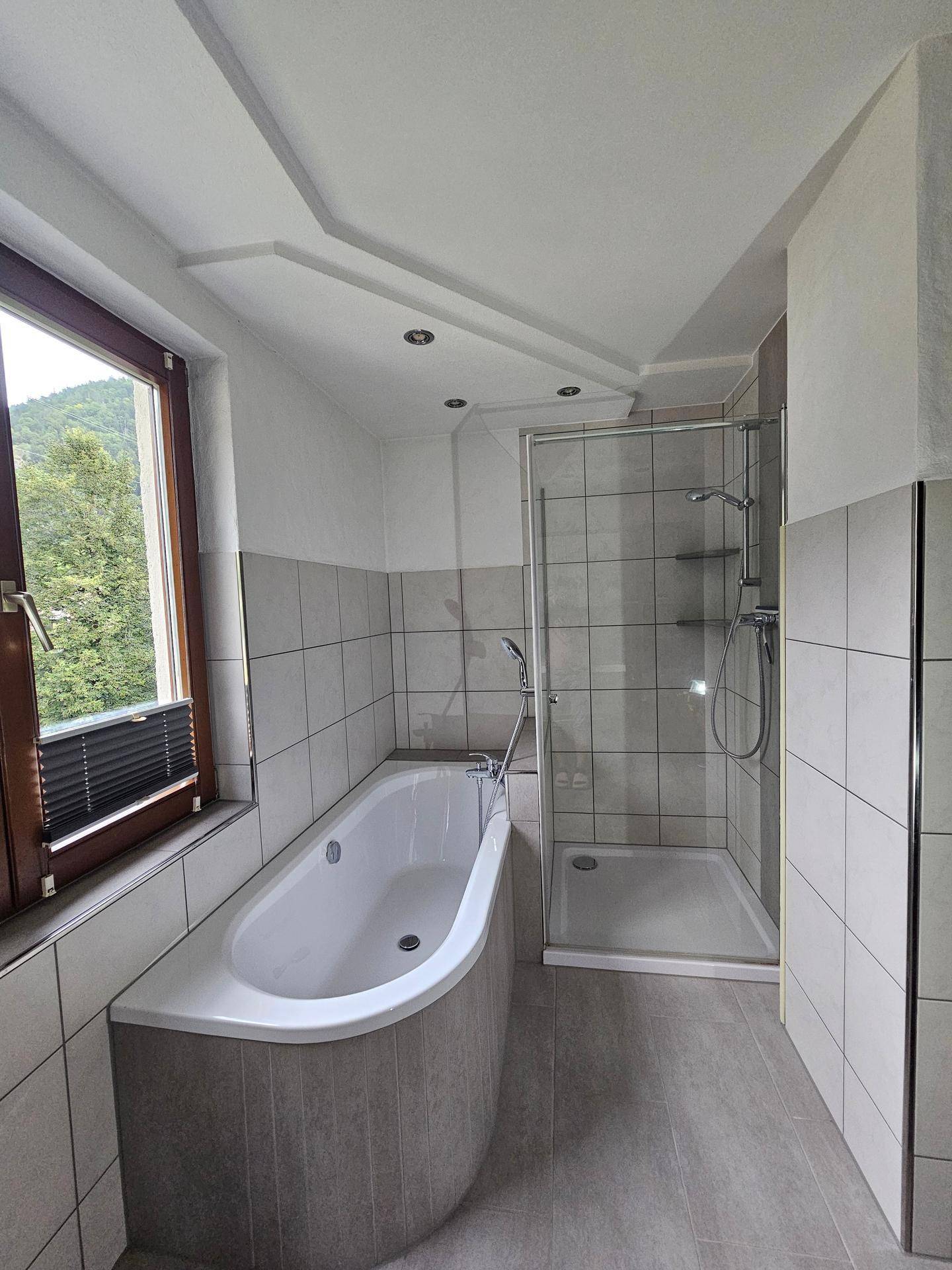 Helles Badezimmer mit Badewanne, Duschkabine und modernen Fliesen.