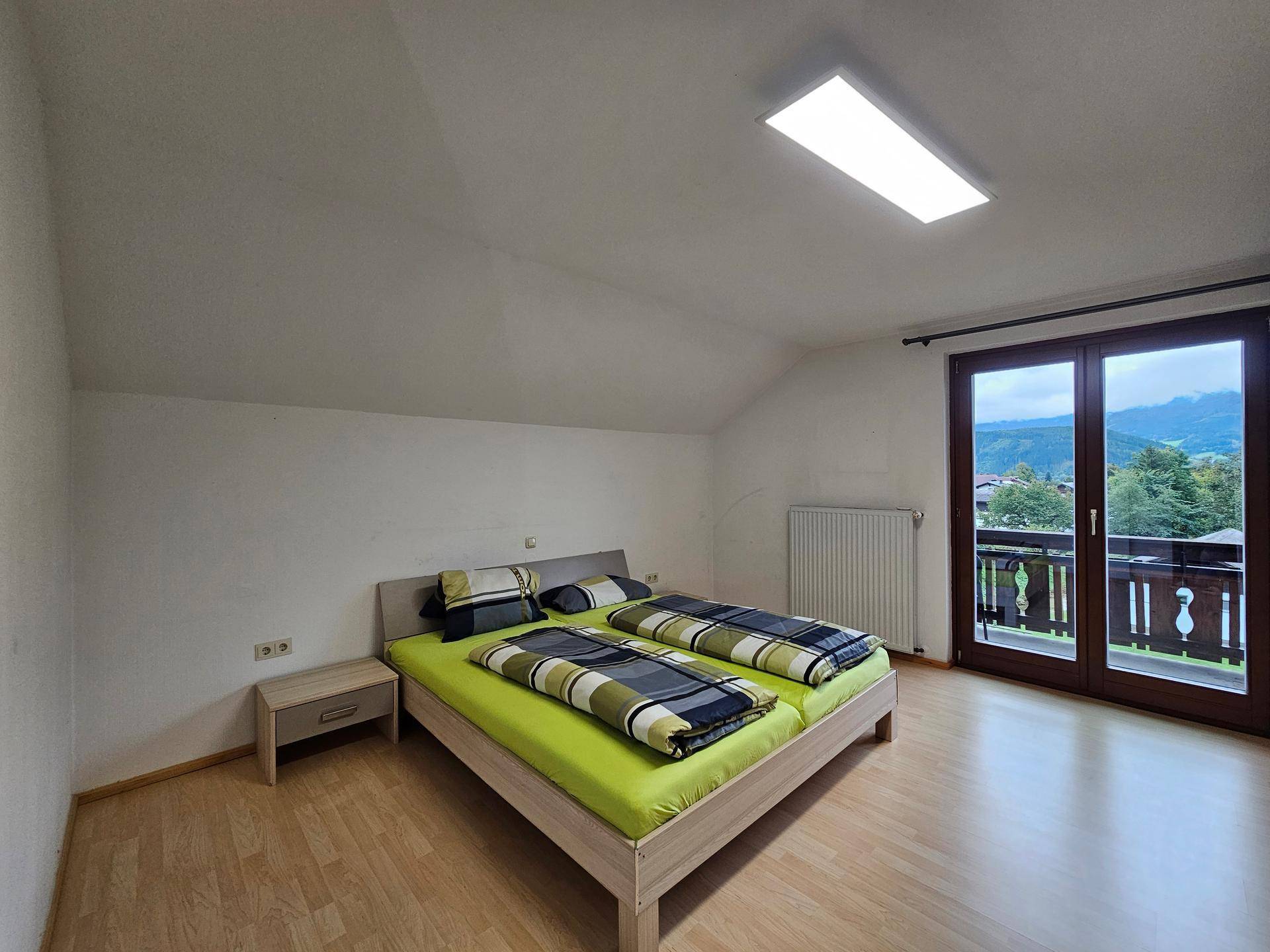 Schlafzimmer mit Doppelbett, Laminatboden und Zugang zum Balkon mit Aussicht.