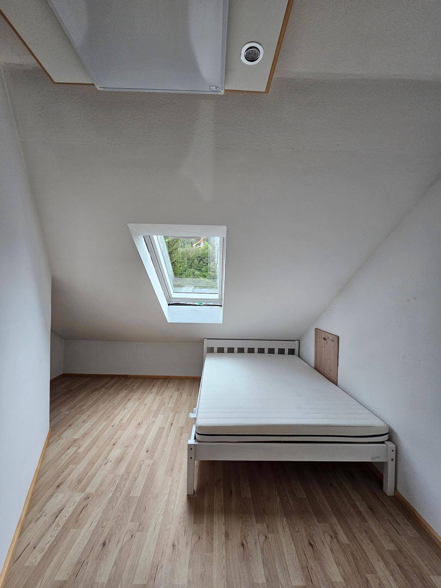 Dachschlafzimmer mit Einzelbett, Laminatboden und Dachfenster für natürliches Licht.
