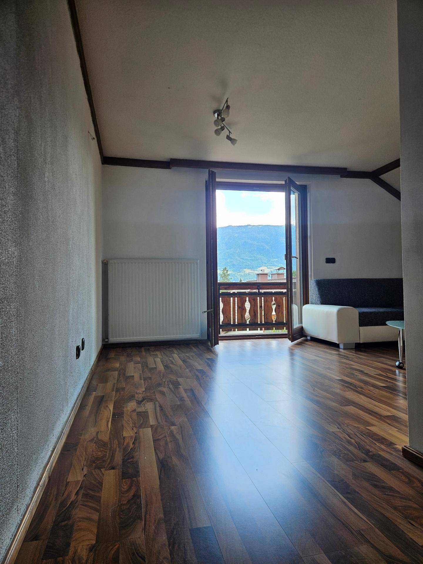 Helles Wohnzimmer mit Laminatboden und Zugang zu einem Balkon mit Bergblick.