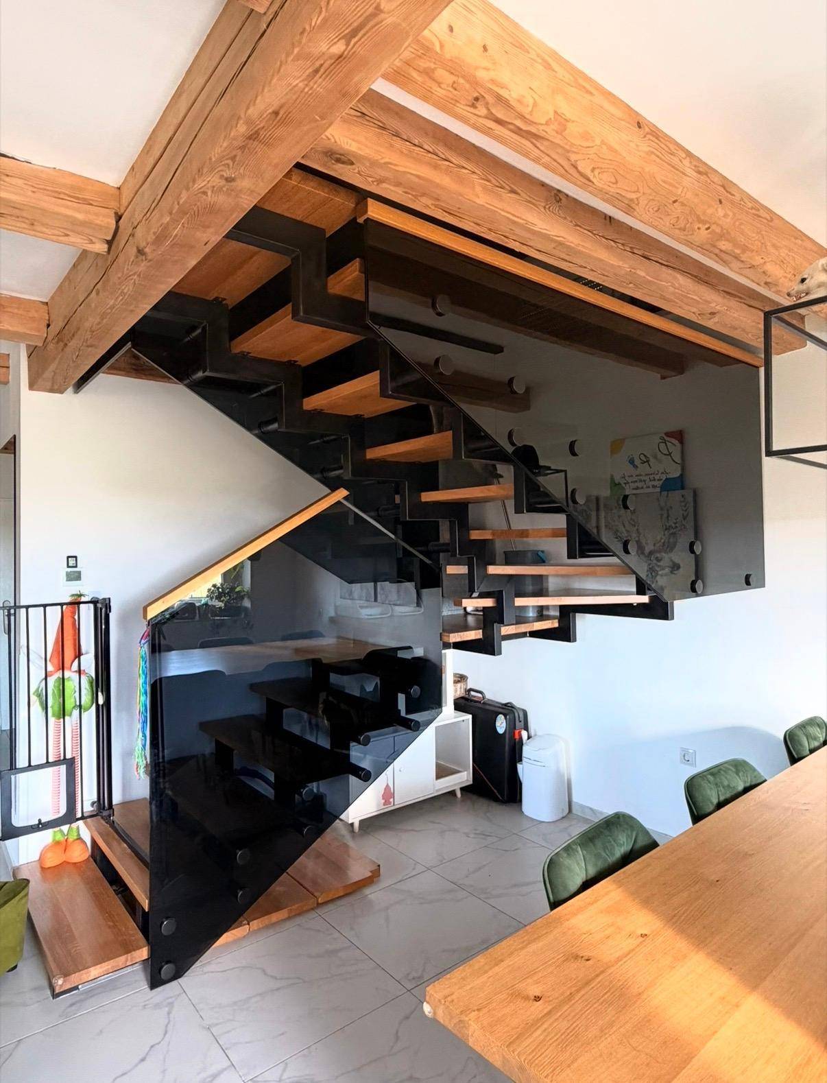 Moderne Treppe mit Glasgeländer und freiliegenden Holzbalken in einem offenen Wohnbereich.