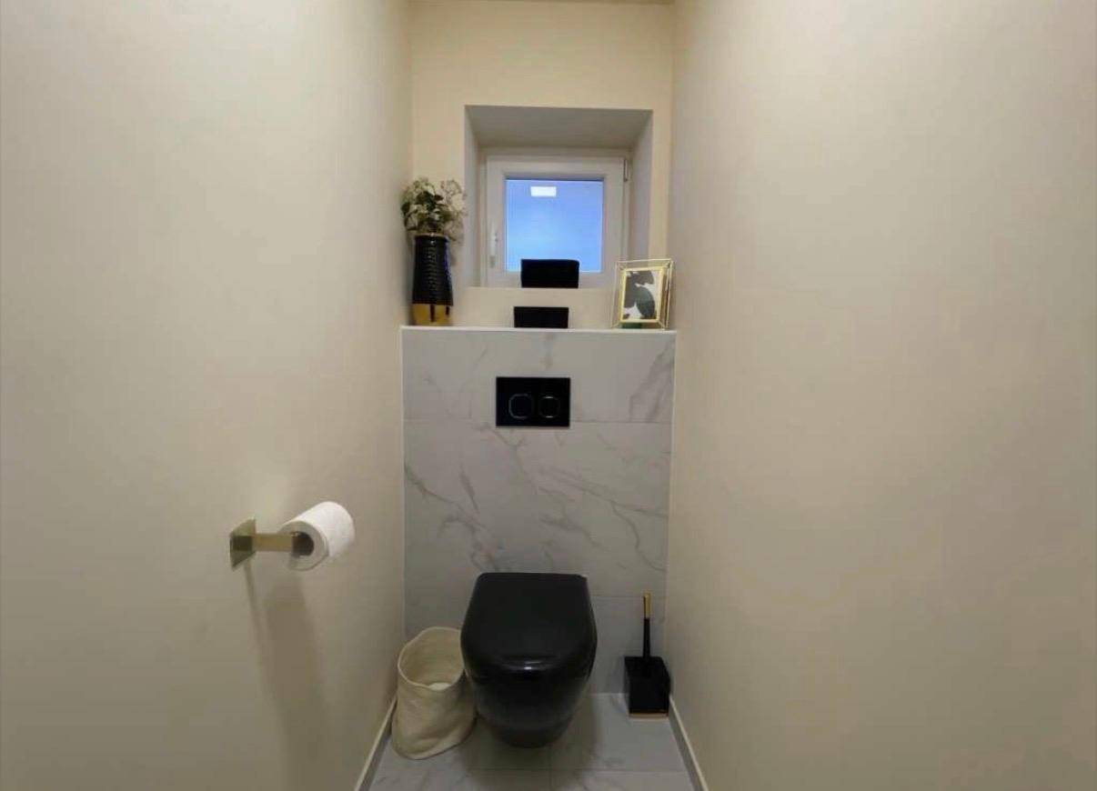 Kleines Gäste-WC mit schwarzer Wandtoilette, modernen Fliesen und einem Fenster.