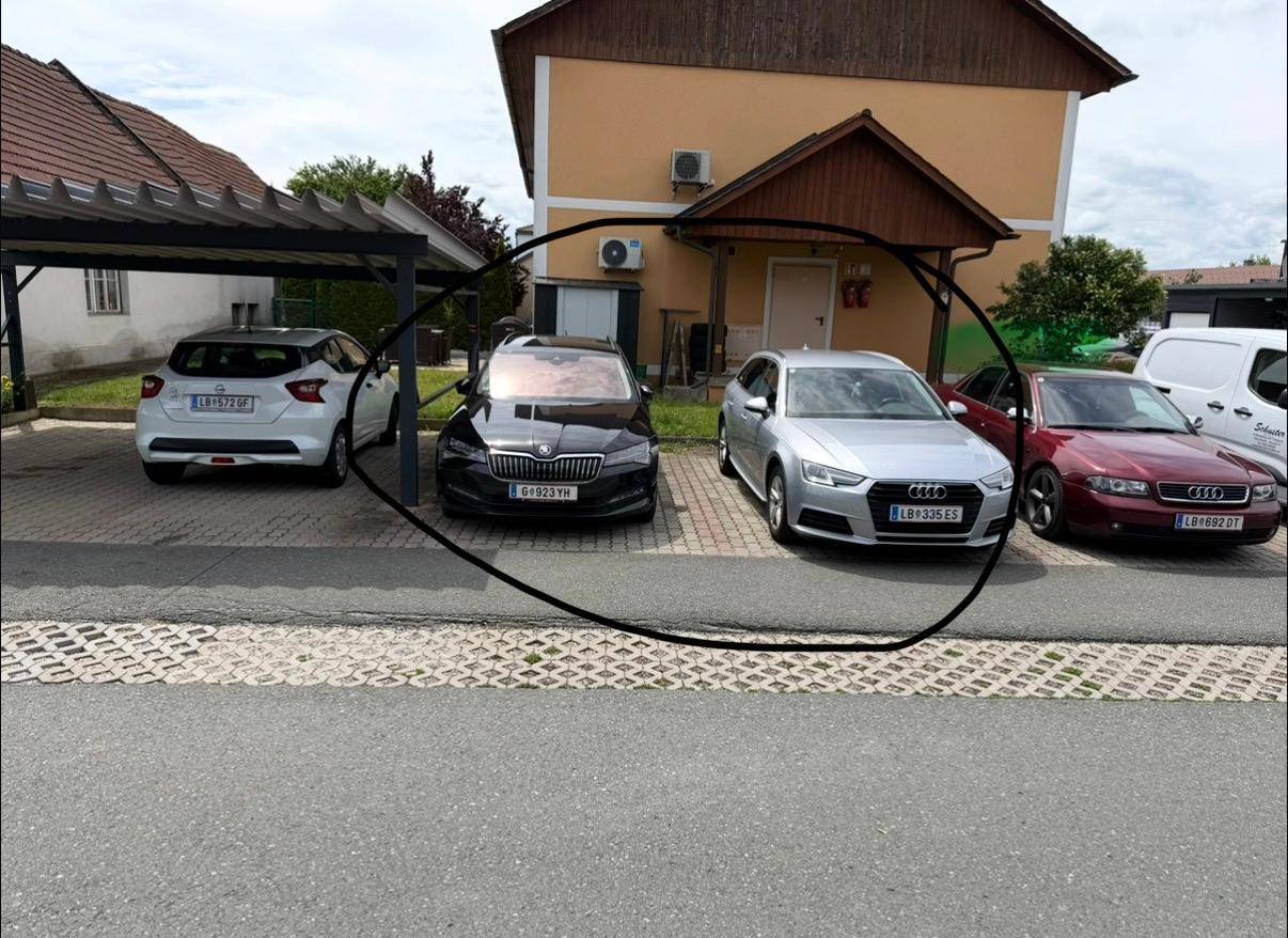Außenansicht des Hauses mit Carport und geparkten Fahrzeugen davor.