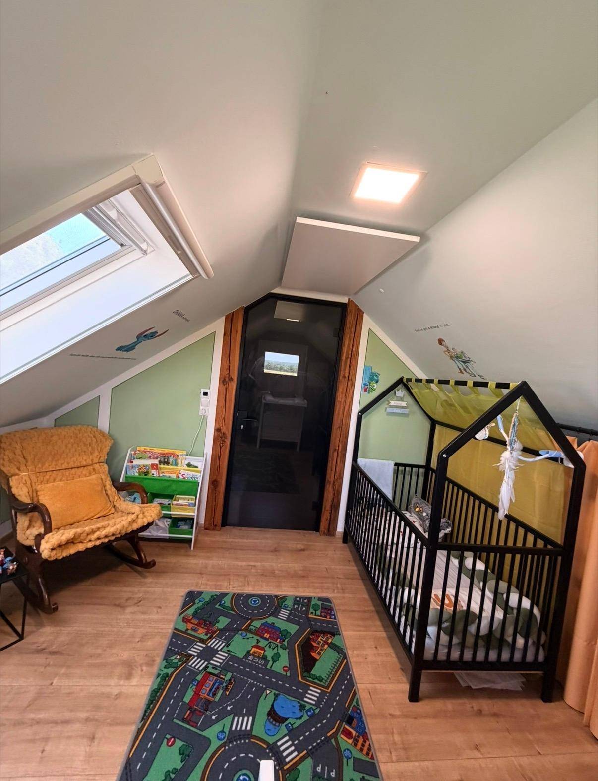 Helles Kinderzimmer im Dachgeschoss mit Babybett, Schaukelstuhl und Dachfenster.