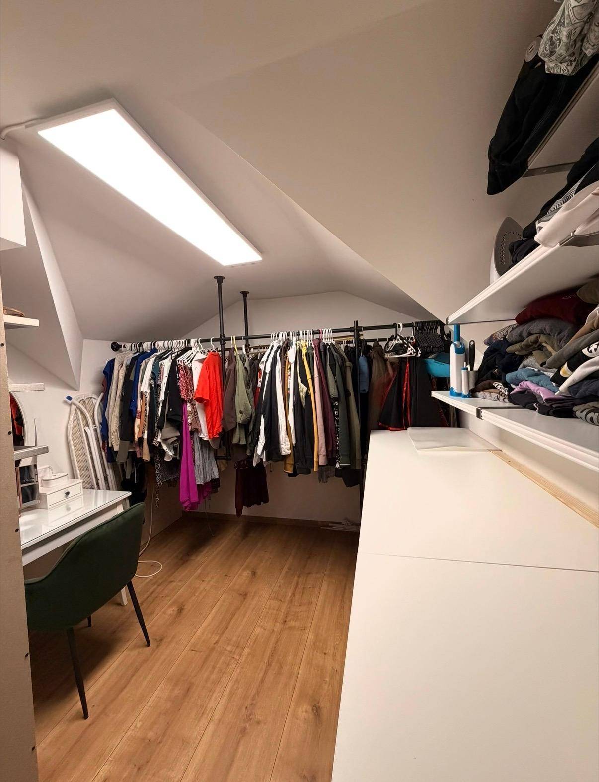 Begehbarer Kleiderschrank im Dachgeschoss mit Kleiderstangen, Regalen und Schreibtisch.
