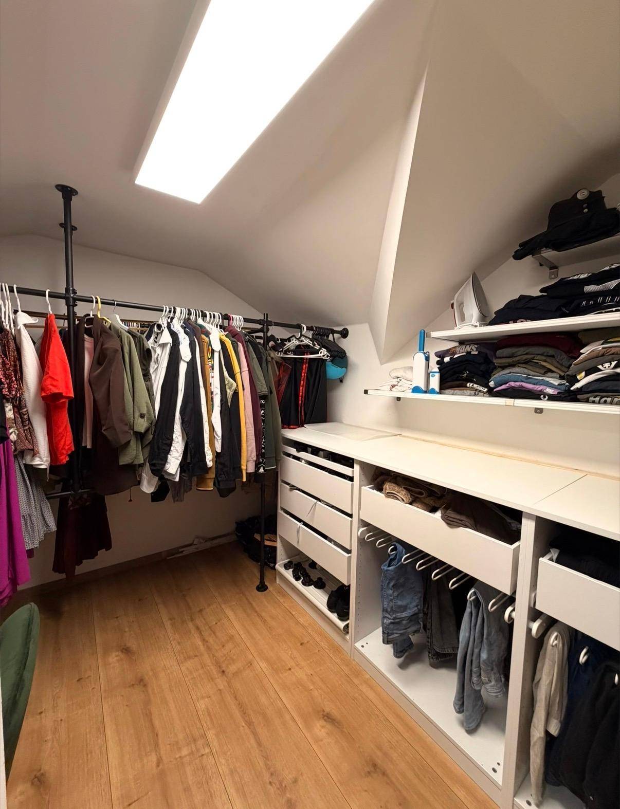 Begehbarer Kleiderschrank im Dachgeschoss mit Kleiderstangen, Regalen und Dachfenster.