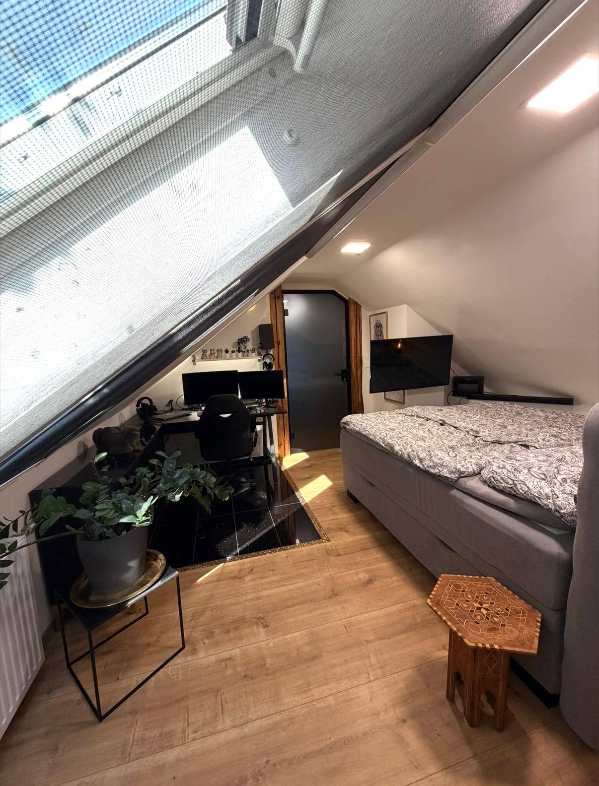 Schlafzimmer im Dachgeschoss mit Bett, Schreibtisch und großem Dachfenster mit Beschattung.