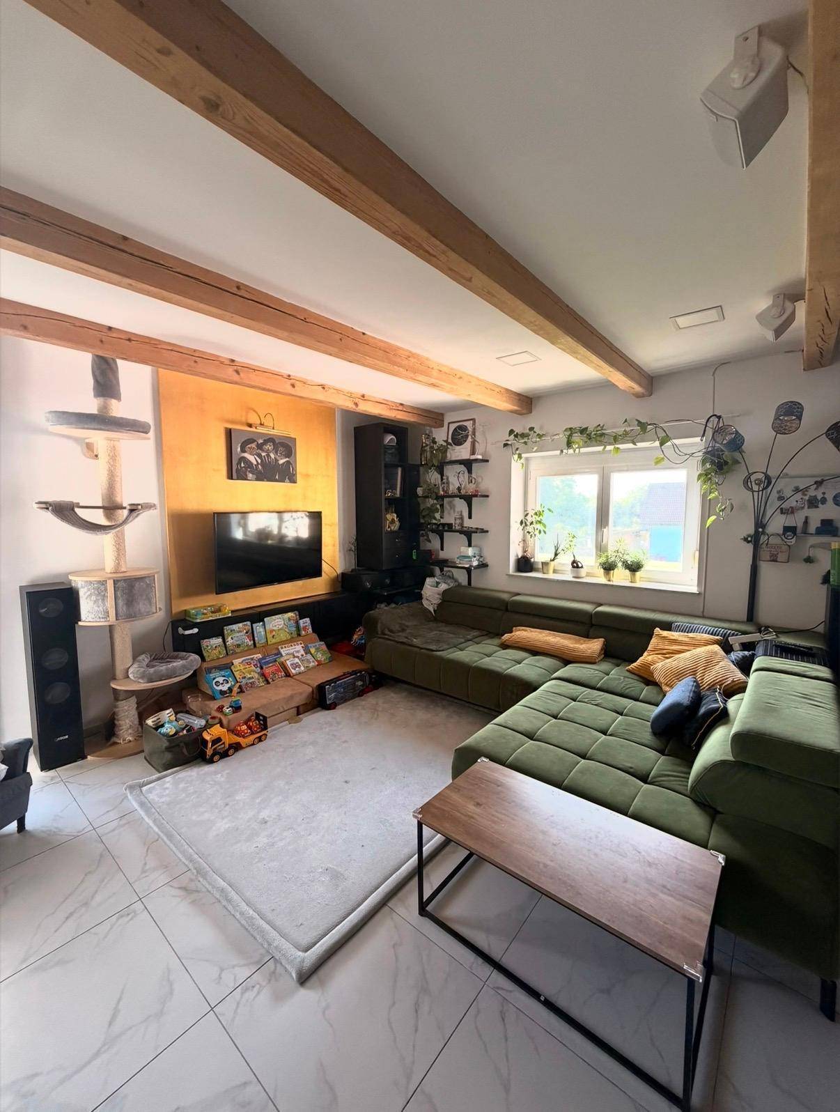 Gemütliches Wohnzimmer mit großer grüner Couch, Fernseher und sichtbaren Holzbalken.