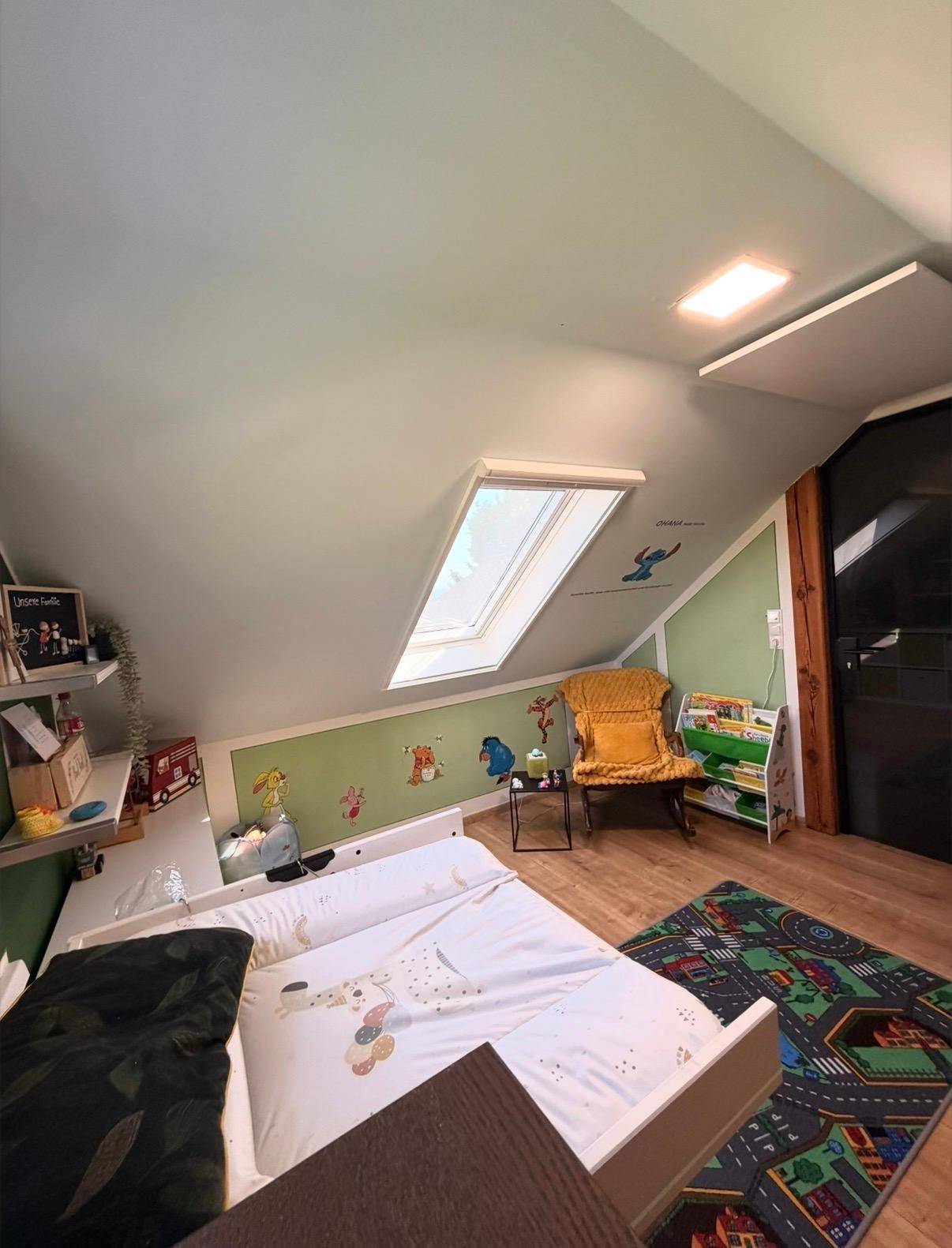 Helles Kinderzimmer im Dachgeschoss mit Bett, Regalen und großem Dachfenster.