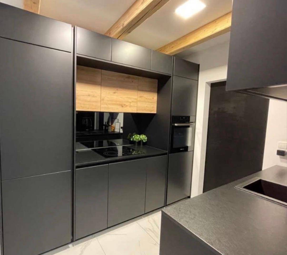 Moderne schwarze Küche mit integrierten Geräten, Induktionskochfeld und Holzbalken.