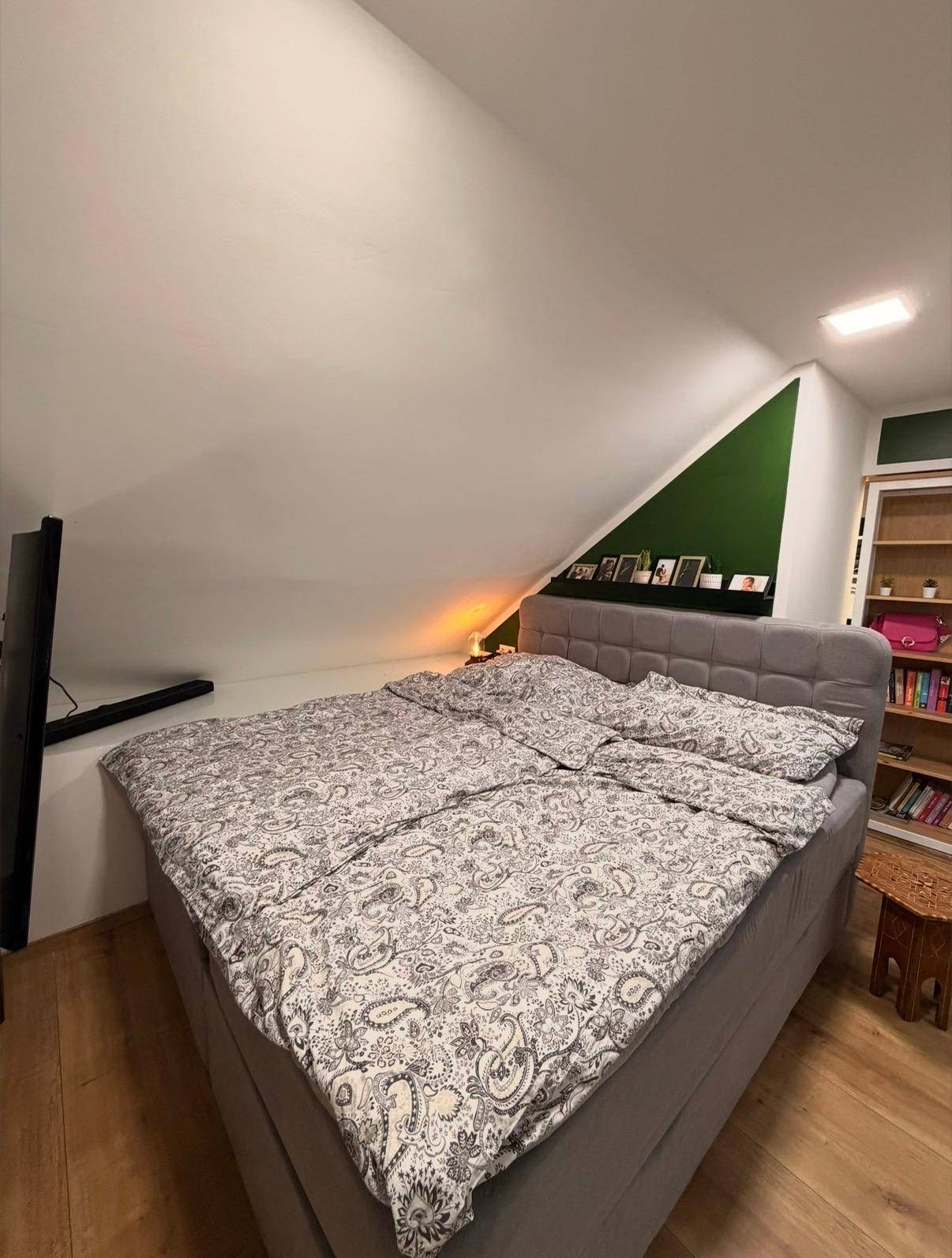 Gemütliches Schlafzimmer im Dachgeschoss mit großem Bett und grüner Akzentwand.