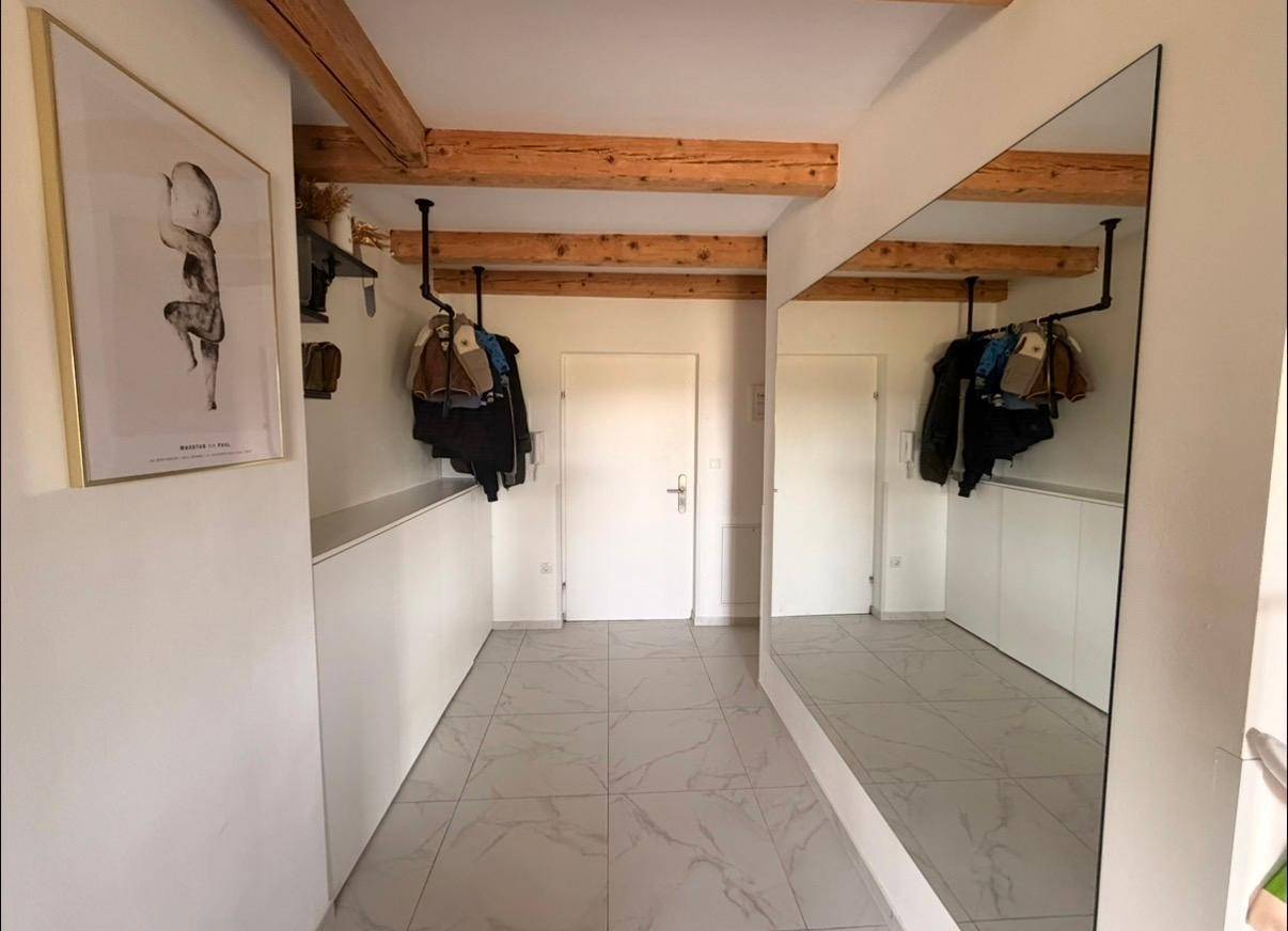 Eingangsbereich mit großem Spiegel, Garderobe und sichtbaren Holzbalken an der Decke.