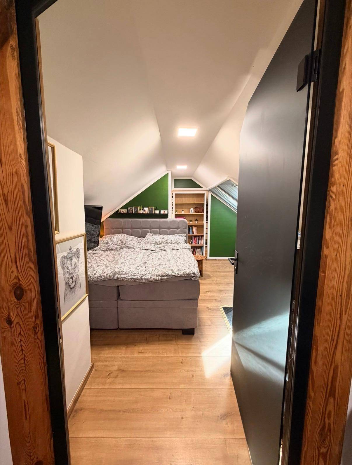 Blick durch eine Tür in ein gemütliches Schlafzimmer im Dachgeschoss mit Holzfußboden.