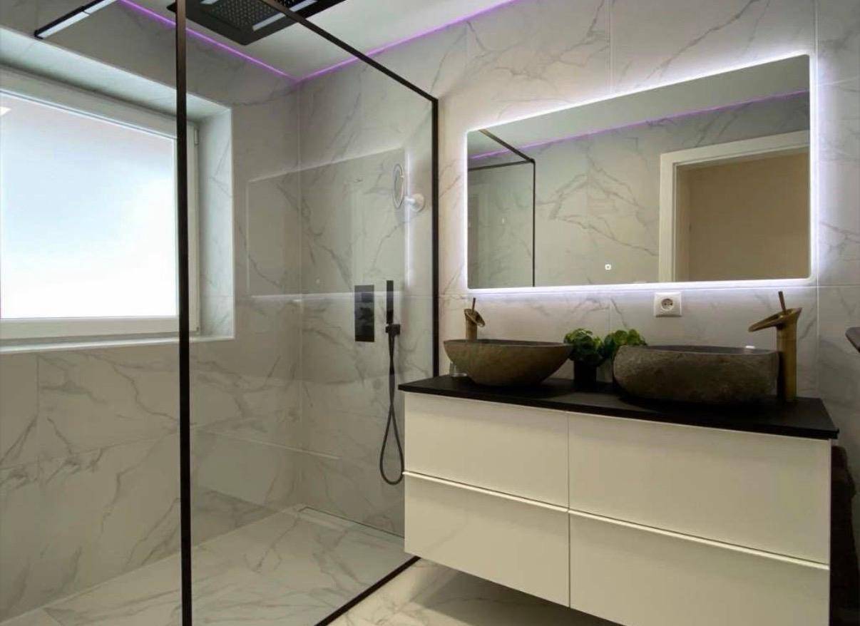 Modernes Badezimmer mit begehbarer Dusche, Doppelwaschbecken und beleuchtetem Spiegel.
