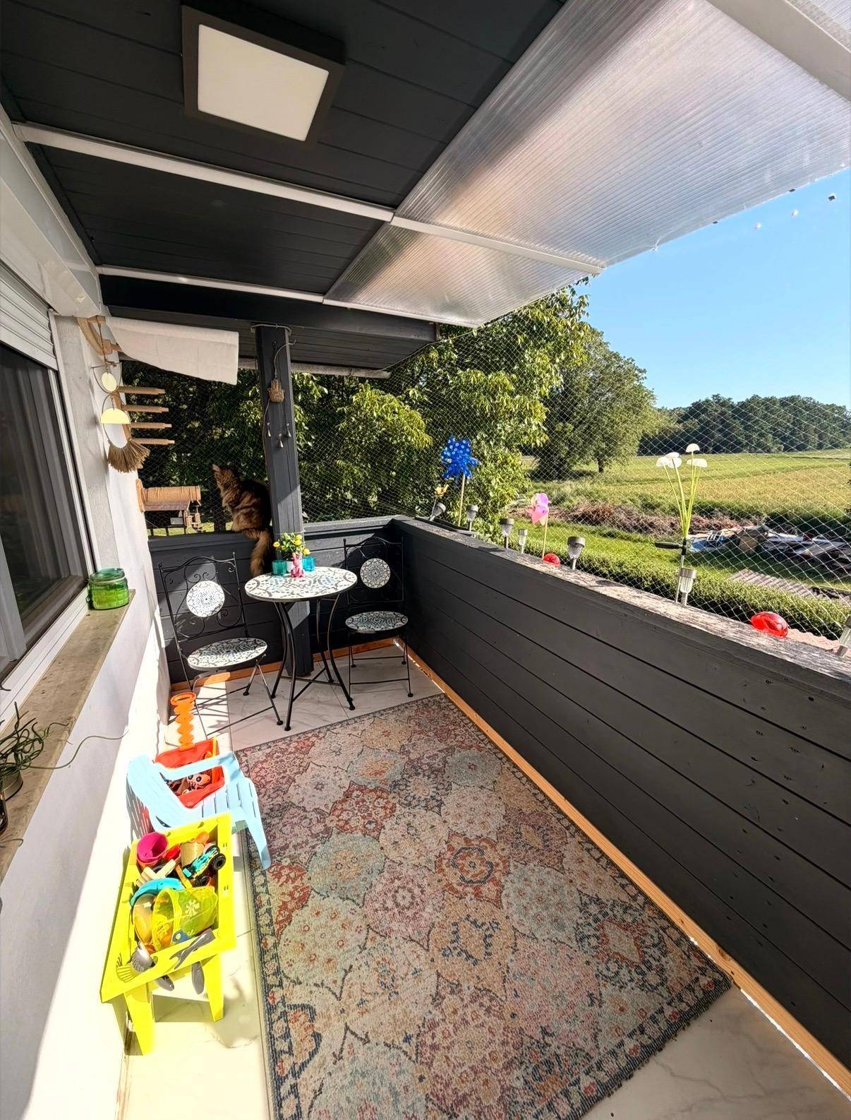 Überdachter Balkon mit Sitzgelegenheiten, Teppich und Blick ins Grüne.