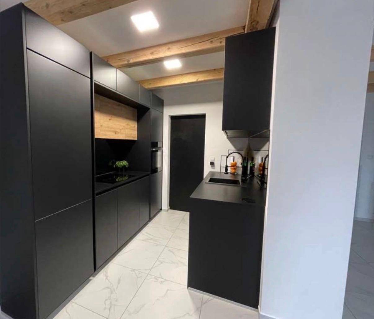 Moderne schwarze Küche mit integrierten Geräten, Holzbalken und weißen Fliesen.