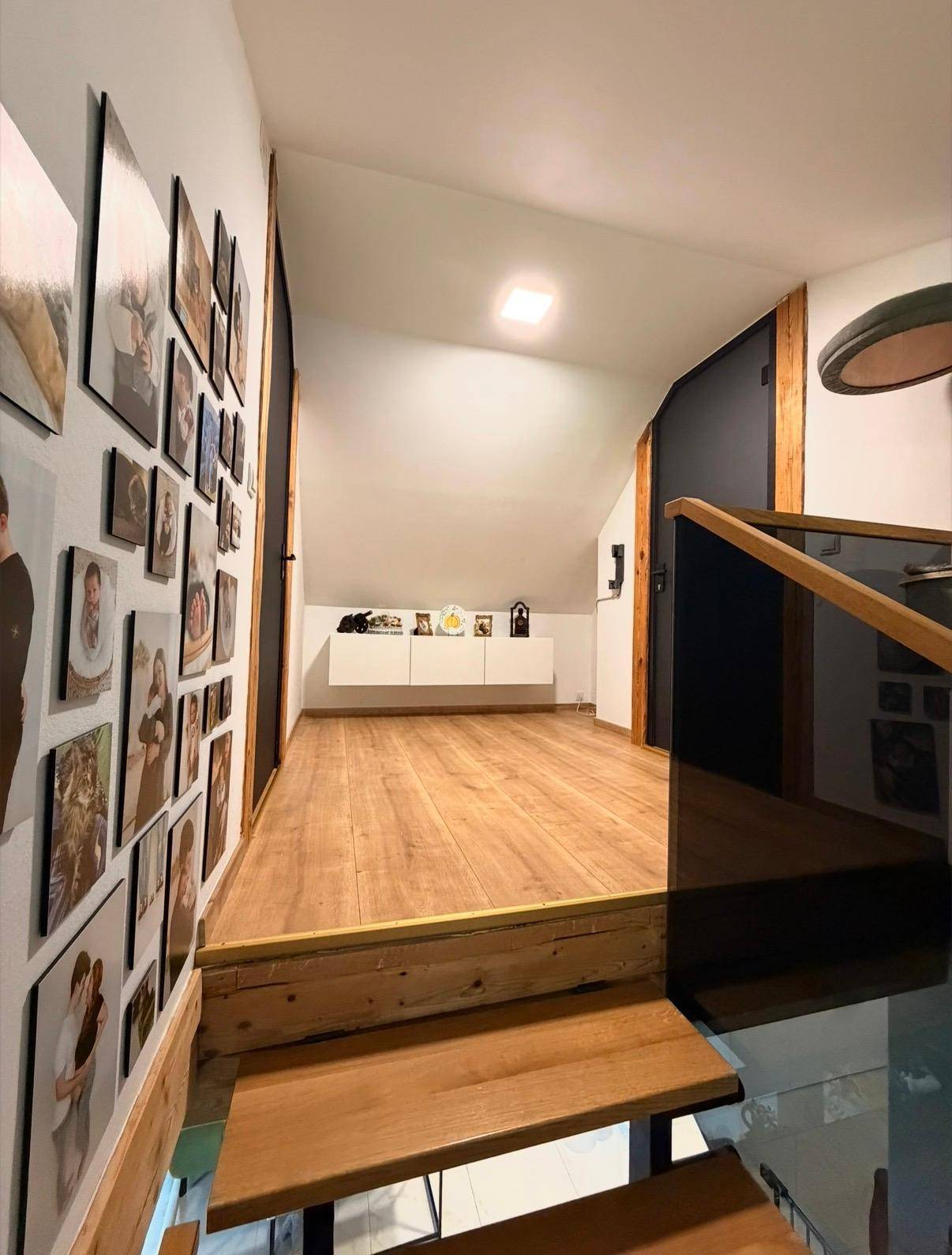 Treppenaufgang zu einem hellen Flur im Dachgeschoss mit vielen Familienfotos an der Wand.