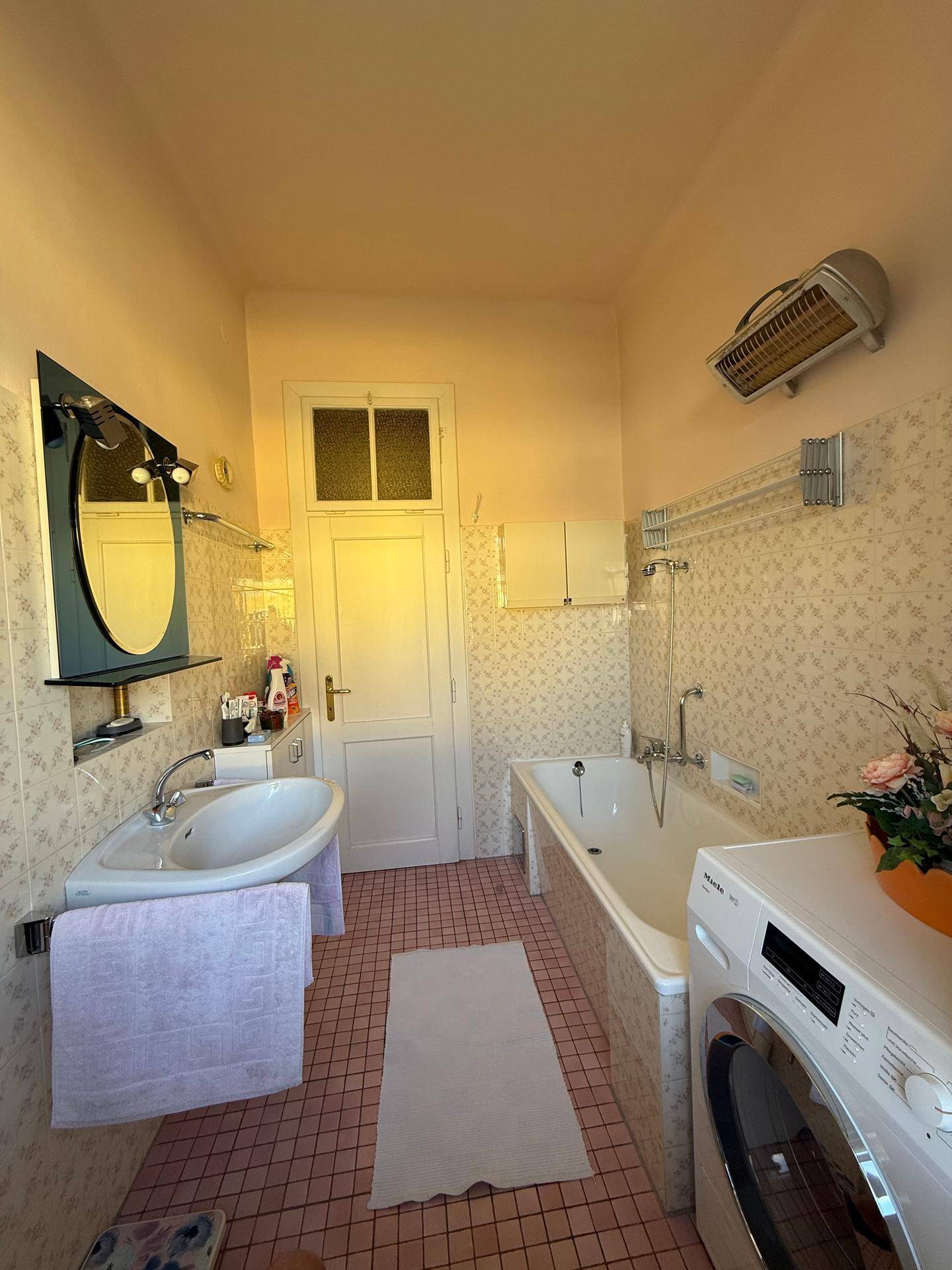 Badezimmer mit Badewanne, Waschbecken und Waschmaschine, ausgestattet mit Fliesen in Pastellfarben.