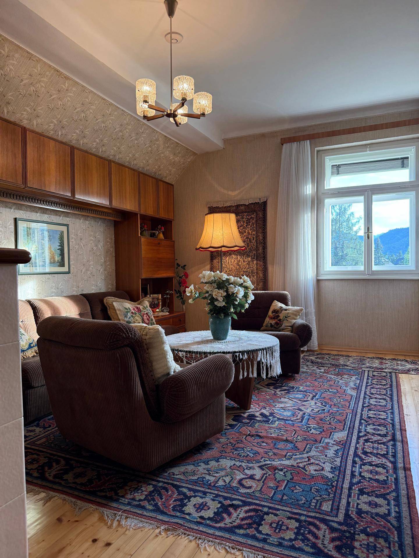 Gemütliches Wohnzimmer mit traditionellen Möbeln, Teppich und Blick auf die grüne Umgebung.