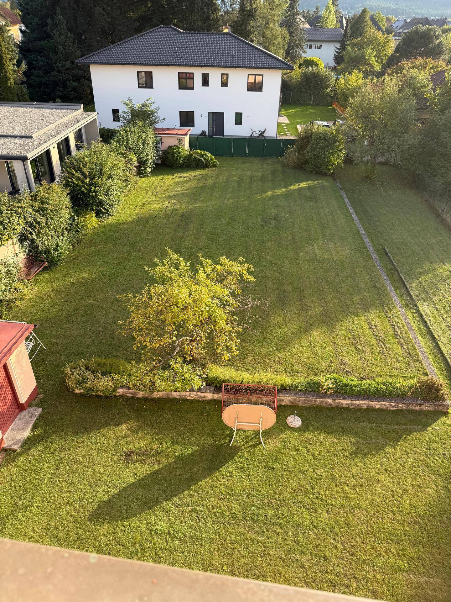 Überblick über den großen Garten mit Rasenfläche, einem Baum und einer kleinen Sitzecke im Freien.