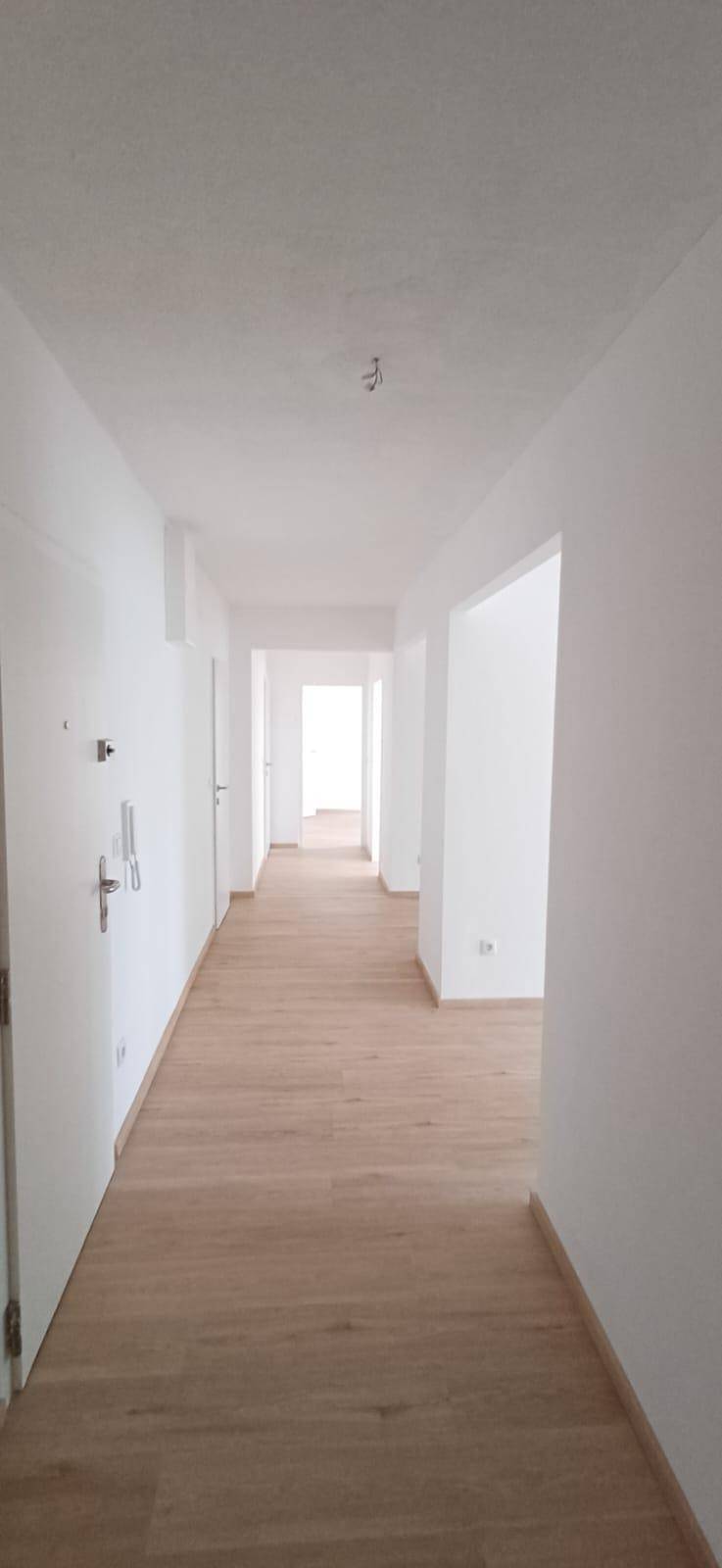 Heller Flur mit hellem Holzboden und weißen Wänden, der zu weiteren Räumen führt.