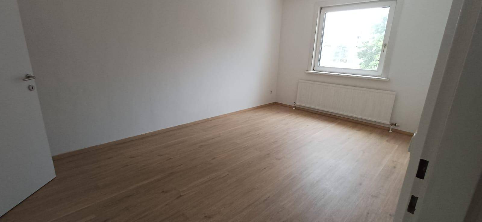 Helles Schlafzimmer mit Holzfußboden, weißen Wänden und Fenster mit Heizkörper, sehr gepflegt.