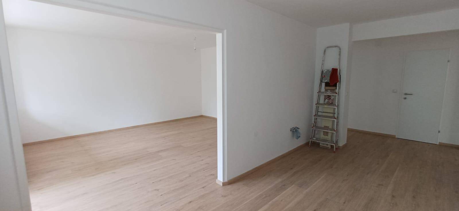 Offener Wohnbereich mit hellem Holzfußboden und weißen Wänden, bereit zur individuellen Gestaltung.
