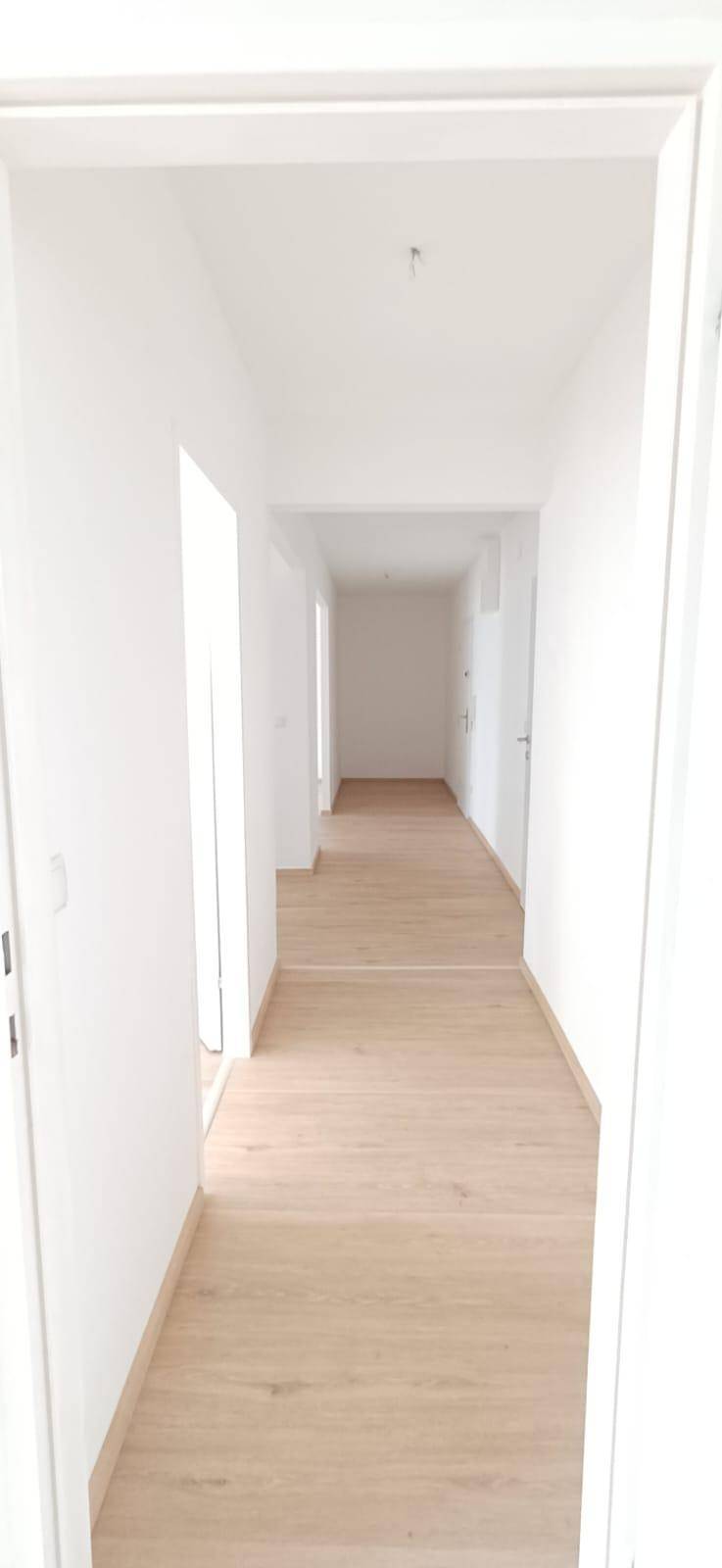 Langer, heller Flur mit neuem Holzfußboden und frisch gestrichenen weißen Wänden, sehr gepflegt.