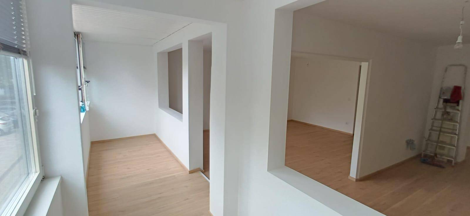 Heller Flur mit Holzfußboden und großen Fenstern, die einen angenehmen Blick ins Grüne bieten.