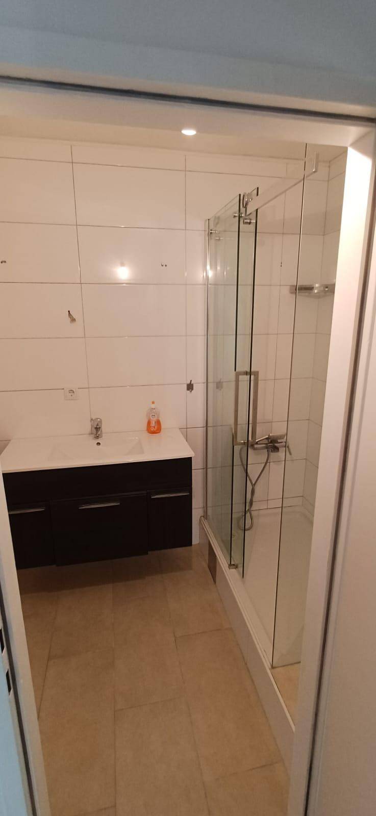 Helles Badezimmer mit weiß gefliesten Wänden, modernem Waschtisch und einer praktischen Glasdusche.