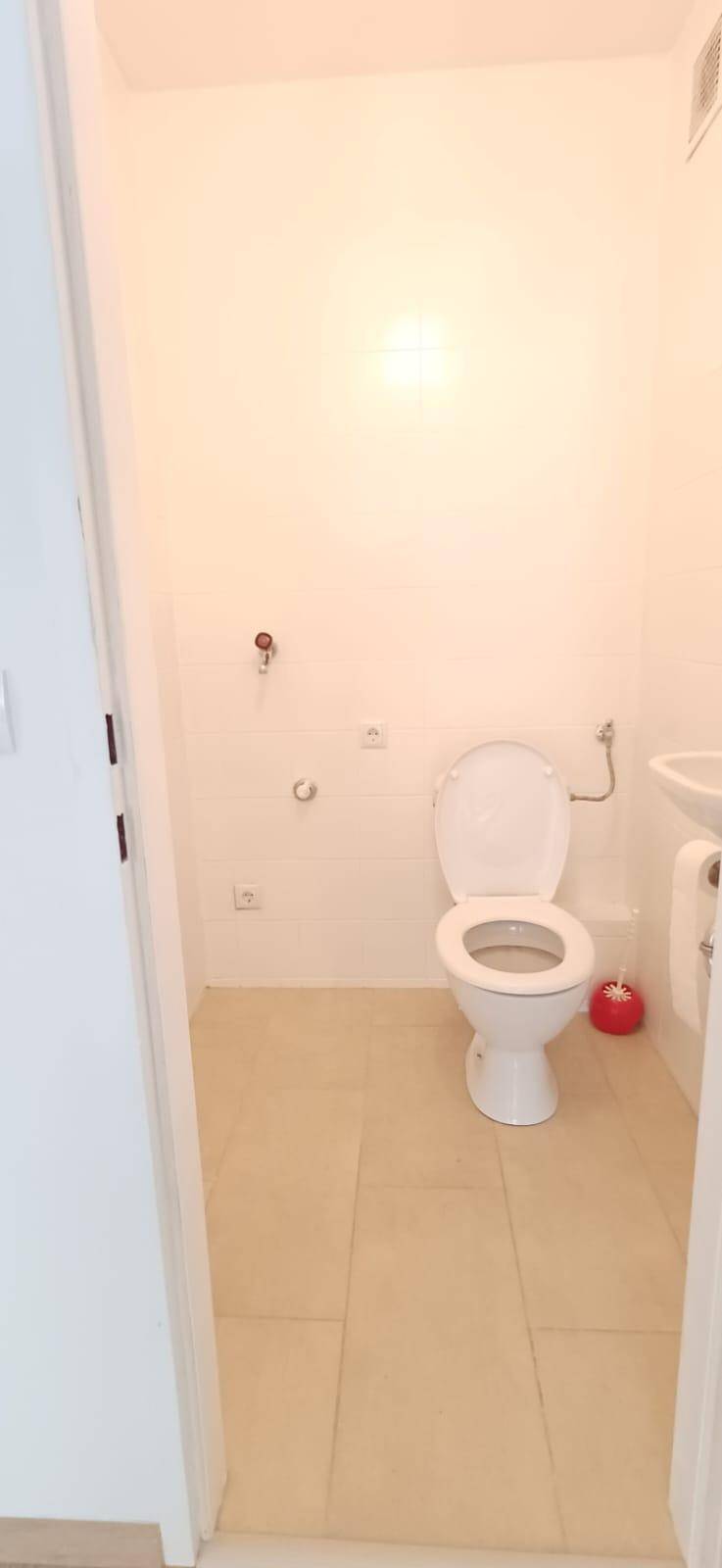 Kleines Gäste-WC mit weißer Toilette, Waschbecken und hellen Fliesen.
