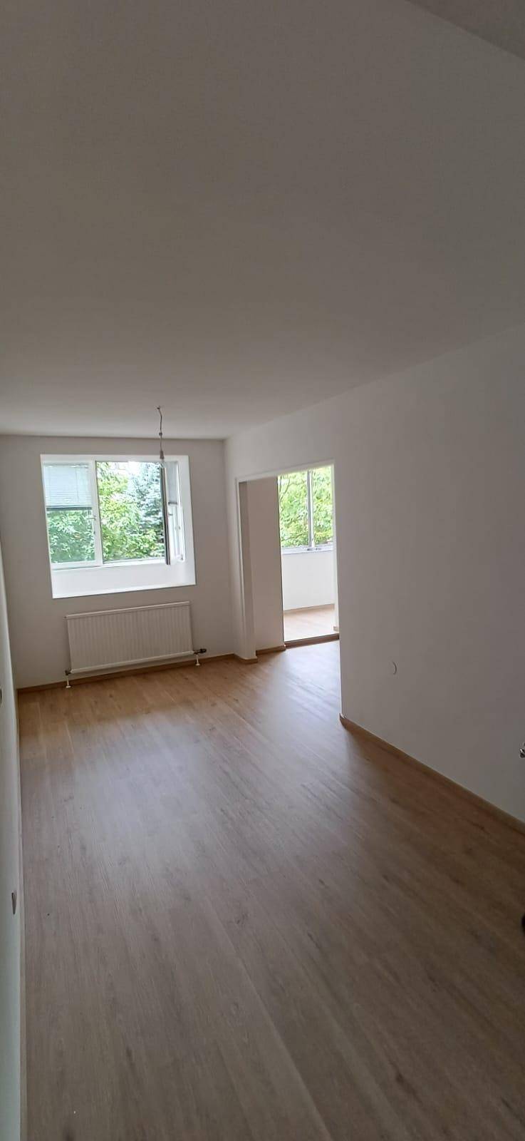 Geräumiges, helles Wohnzimmer mit Holzfußboden und Zugang zu einem verglasten Balkon.