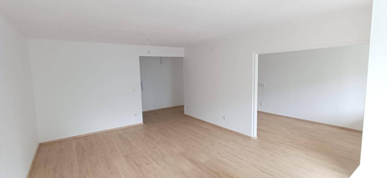 Offener Wohnbereich mit hellem Holzfußboden und weißen Wänden, bereit zur individuellen Gestaltung.