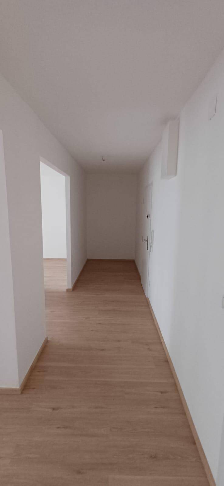 Langer, heller Flur mit neuem Holzfußboden und frisch gestrichenen weißen Wänden, sehr gepflegt.