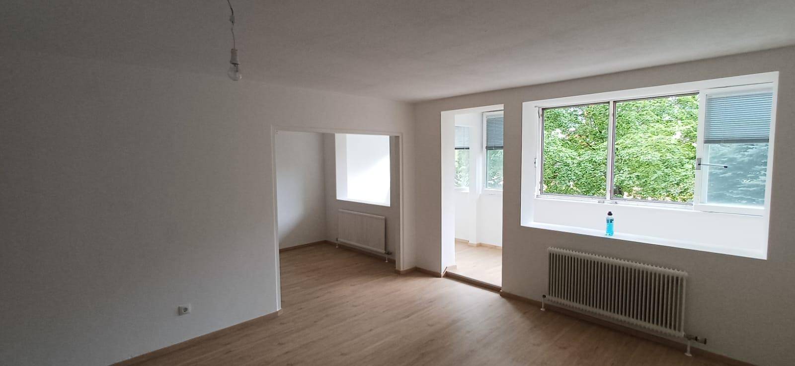 Geräumiges, helles Wohnzimmer mit Holzfußboden und Zugang zu einem verglasten Balkon.