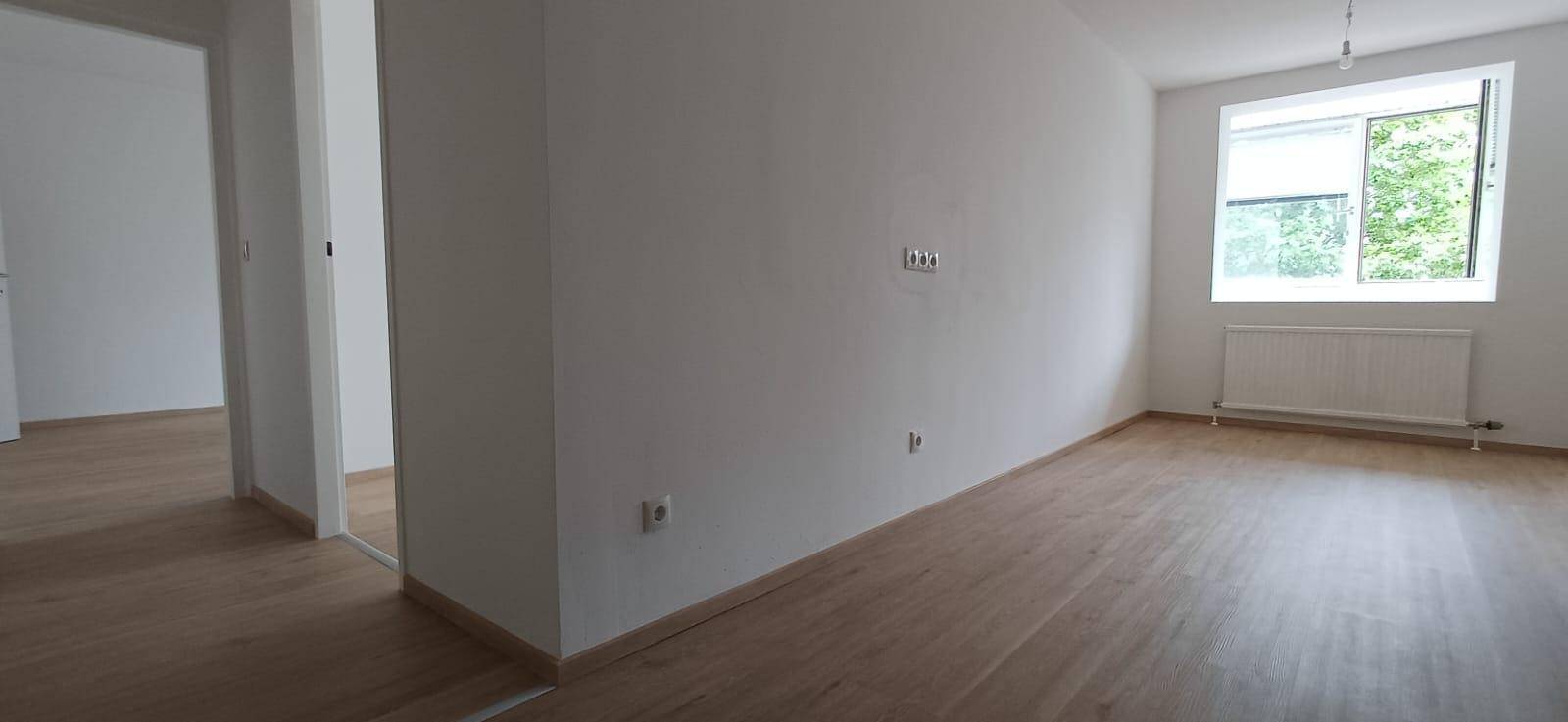 Geräumiges, helles Zimmer mit Holzfußboden, weißen Wänden und einem Fenster mit Blick ins Grüne.