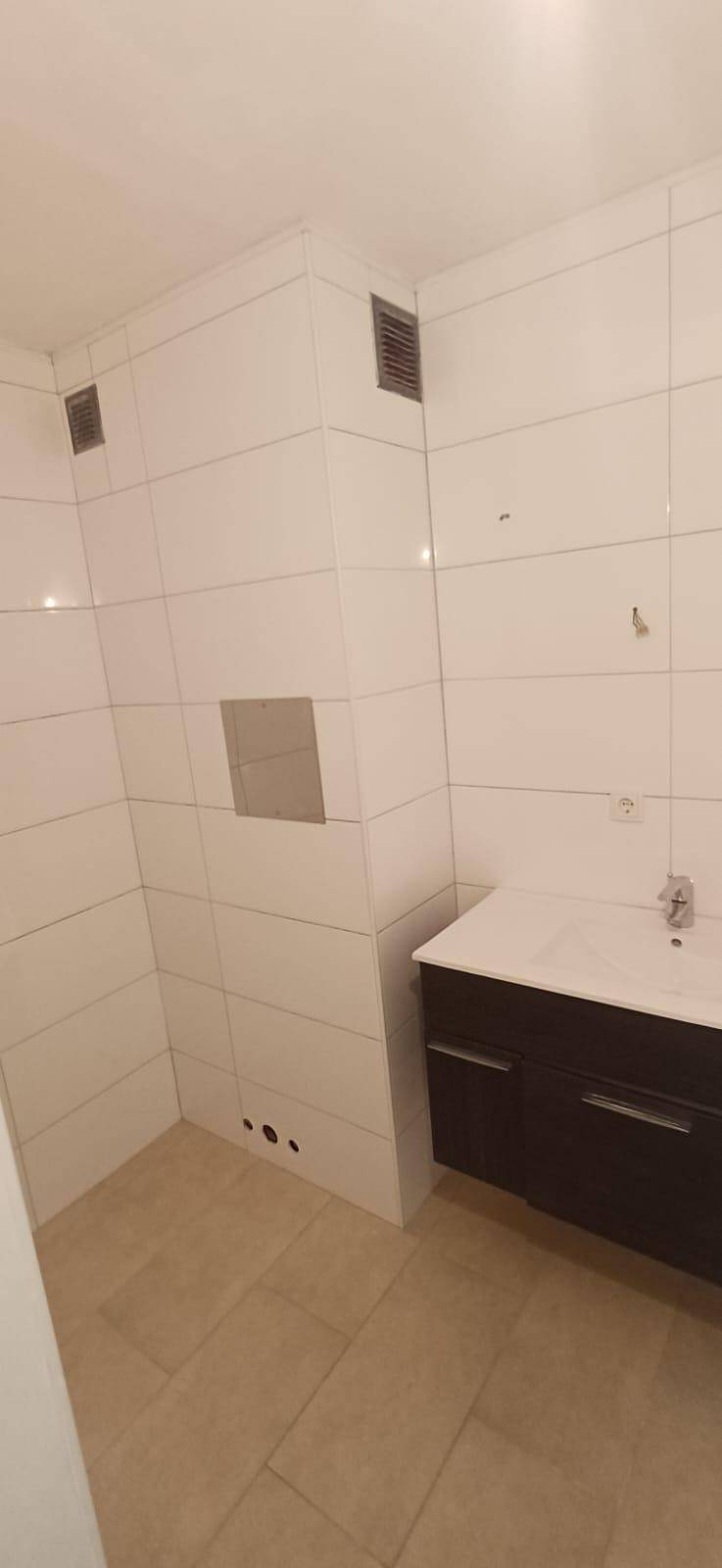 Modern gefliestes Badezimmer mit dunklem Waschtisch und weißem Einzelwaschbecken, bereit zur Nutzung.