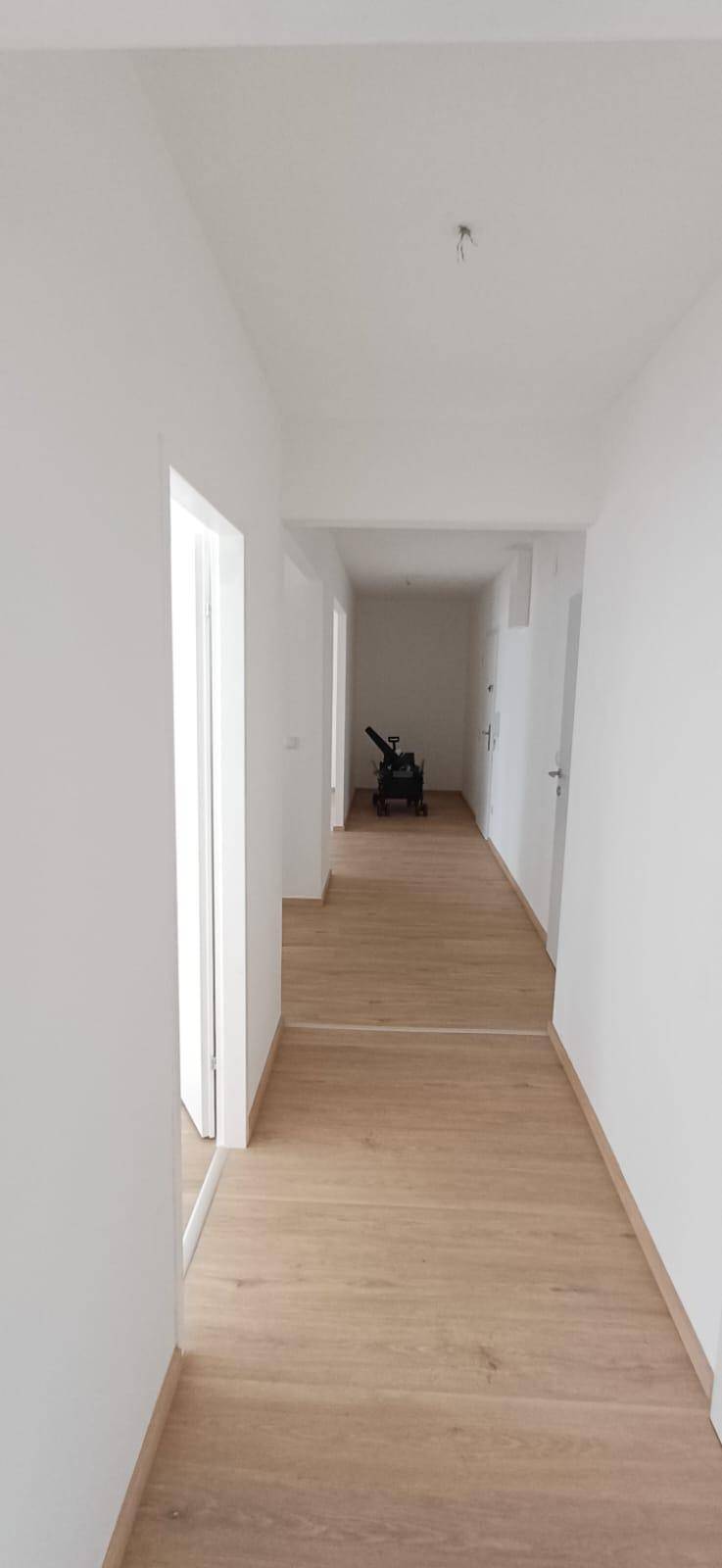 Langer, heller Flur mit Holzfußboden und weißen Wänden, der zu weiteren Räumen führt.