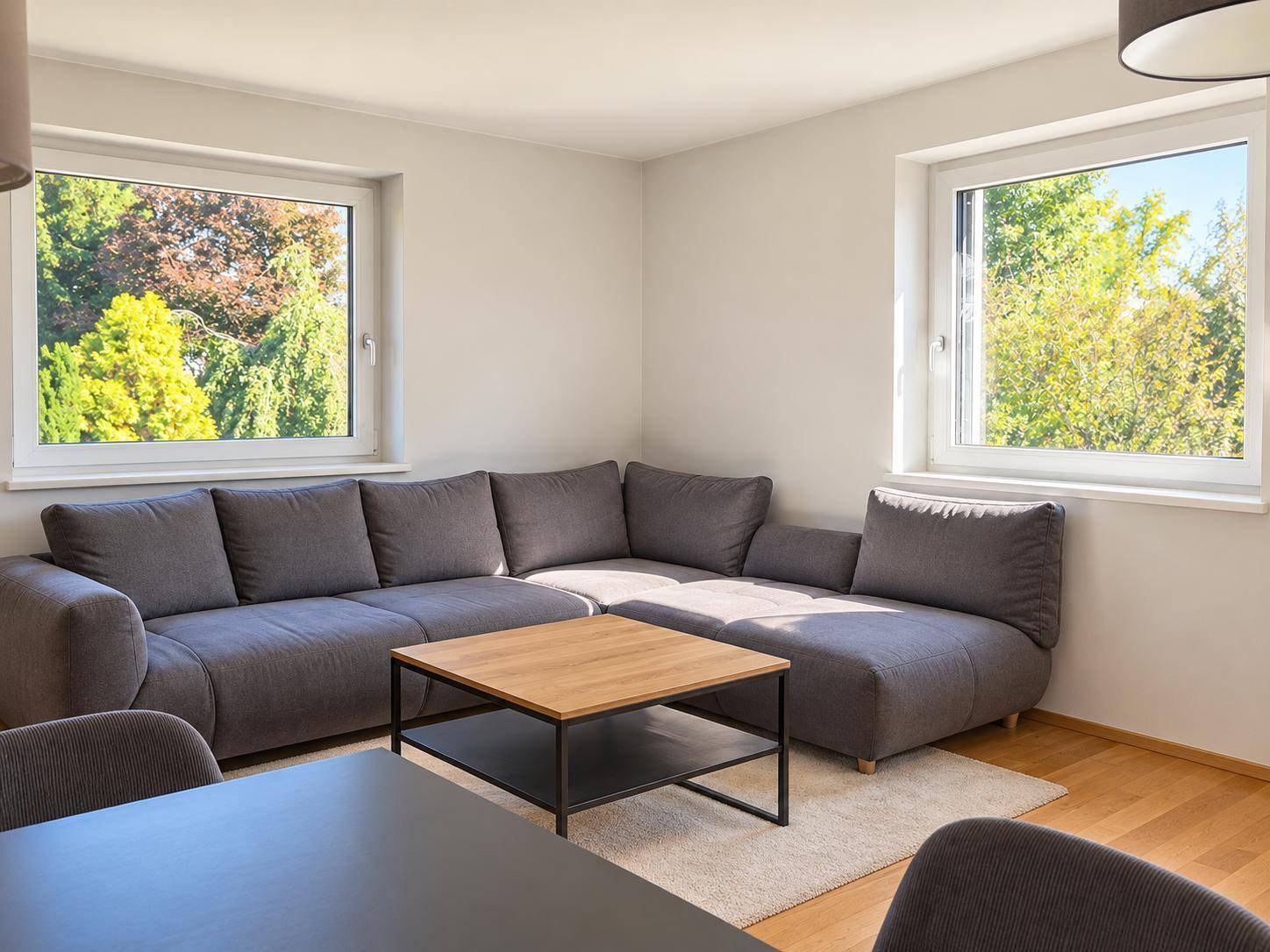 Helles Wohnzimmer mit großem Ecksofa, Laminatboden und Blick ins Grüne.
