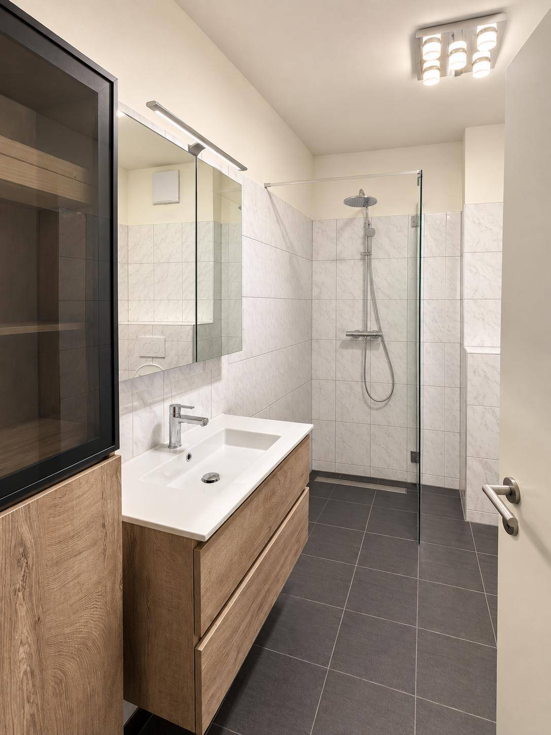 Helles Badezimmer mit modernem Waschtisch, Spiegelschrank und großer Dusche.